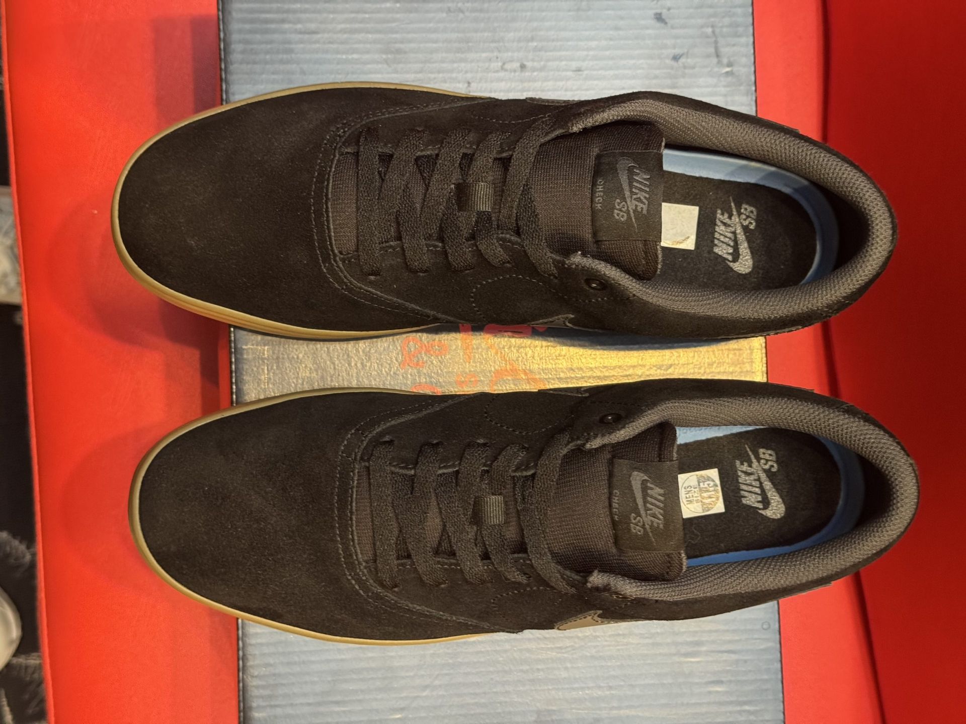 Black Nike sneakers with a gum sole, sitting on a black shoebox, with a red background.