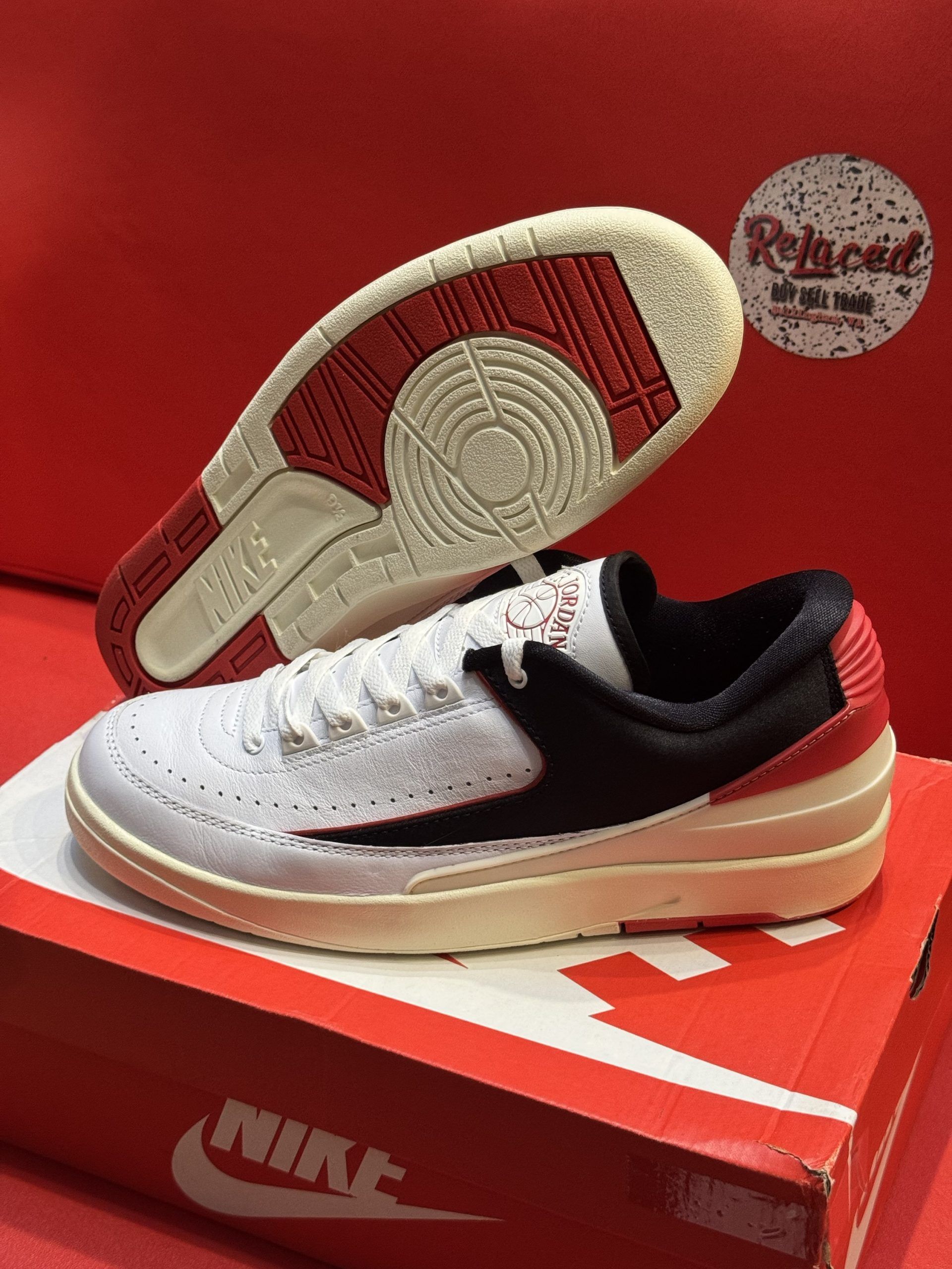 White and black athletic shoe with red accents, placed on a Nike box, with a view of the sole.