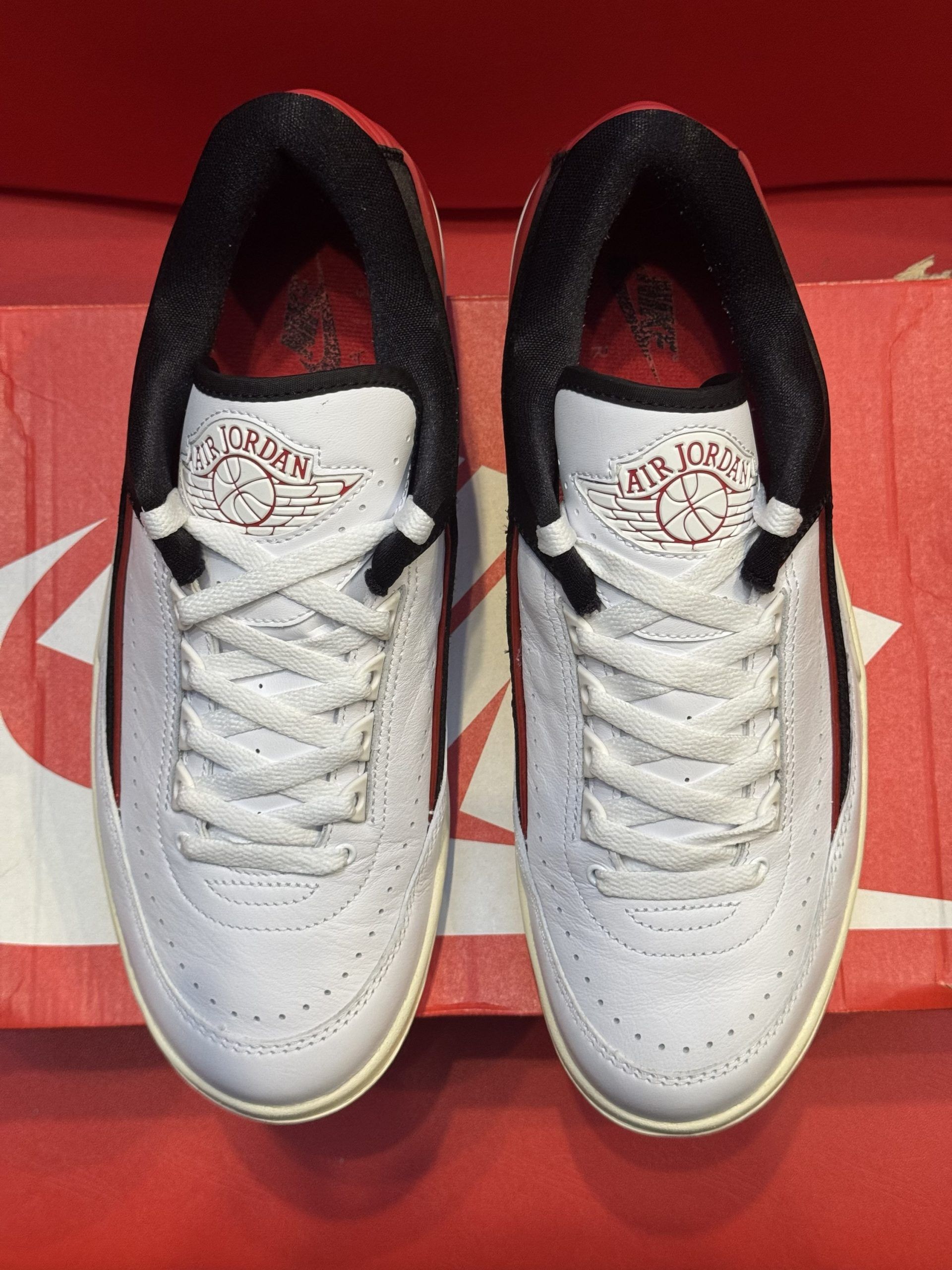 White and black athletic shoe with red accents, placed on a Nike box, with a view of the sole.