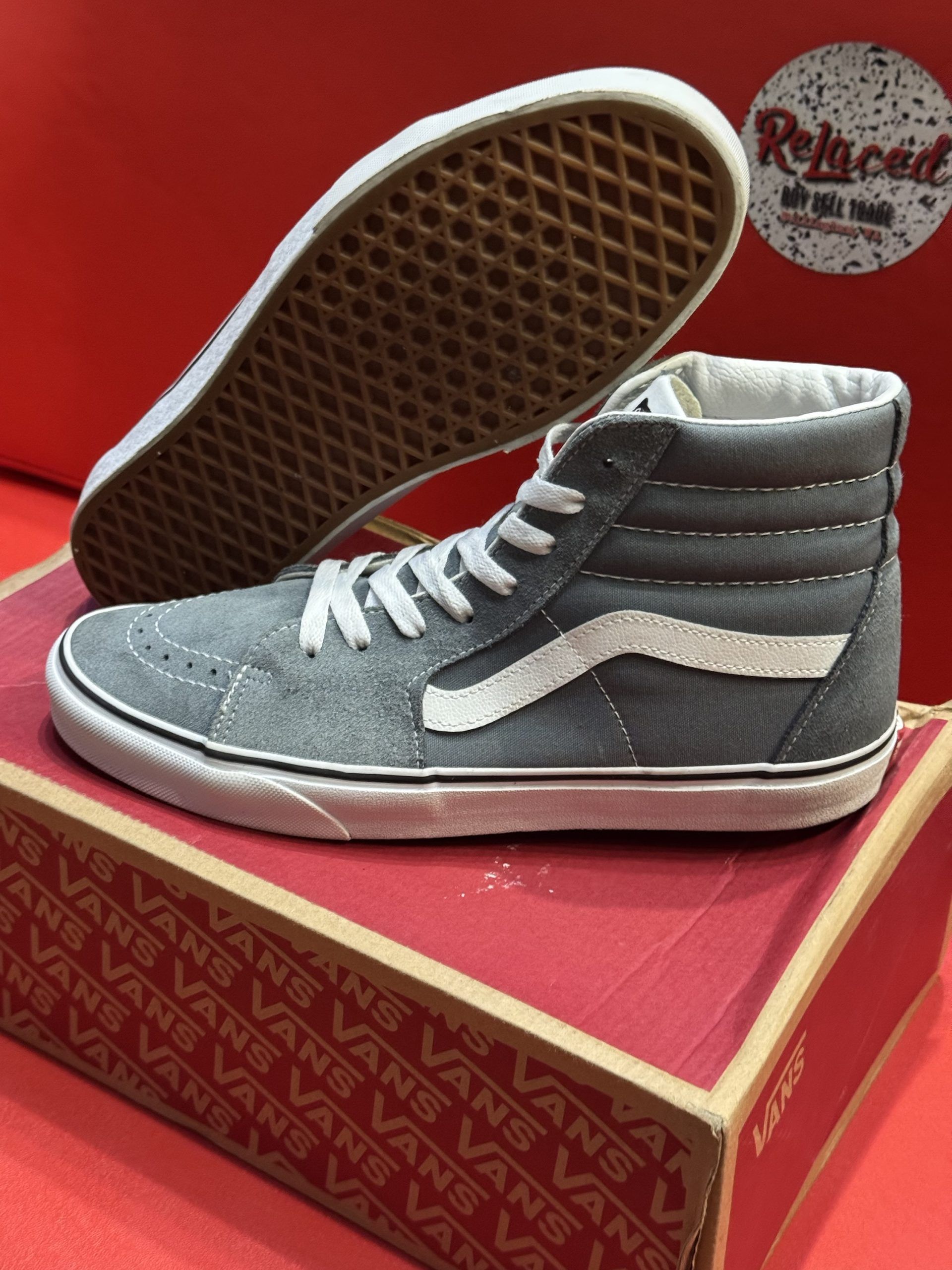 Gray Vans Sk8-Hi sneakers on a shoe box with a red background. The sneakers have white accents and a gum sole.