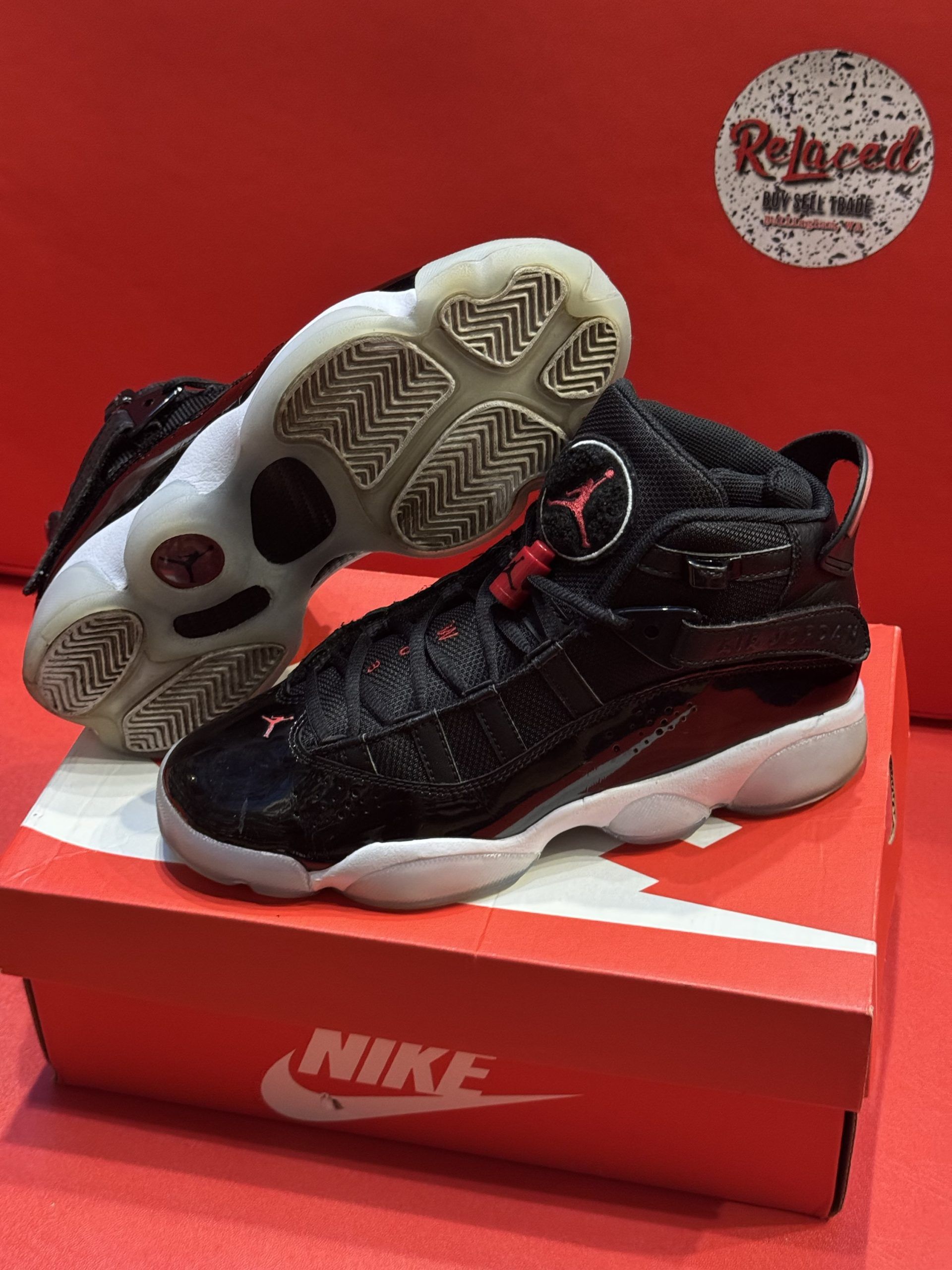 Black and red Air Jordan 6 Rings sneakers on a Nike box, set against a red background.
