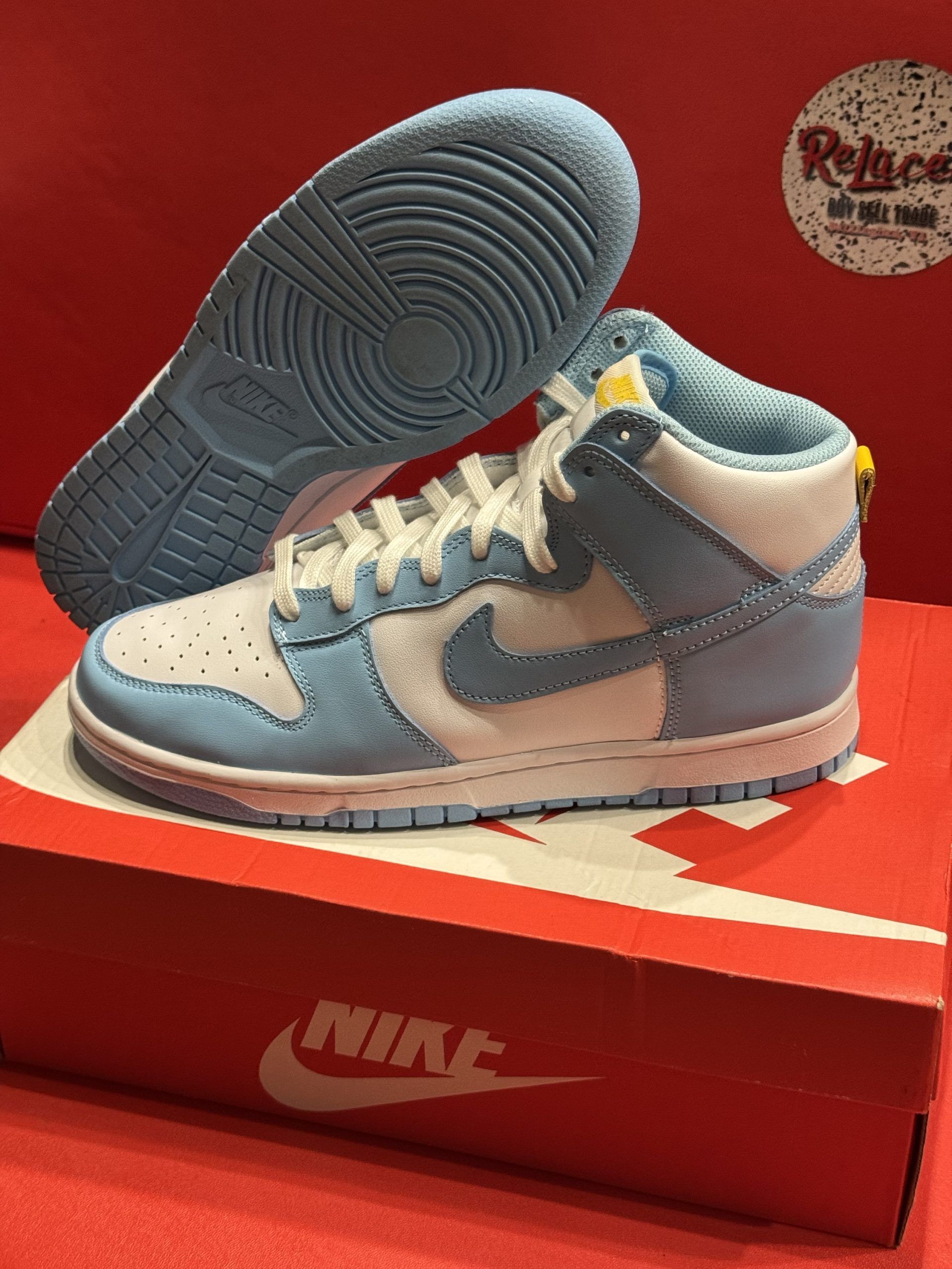 Blue and white Nike Dunk High sneakers on a red Nike box, light blue sole visible.