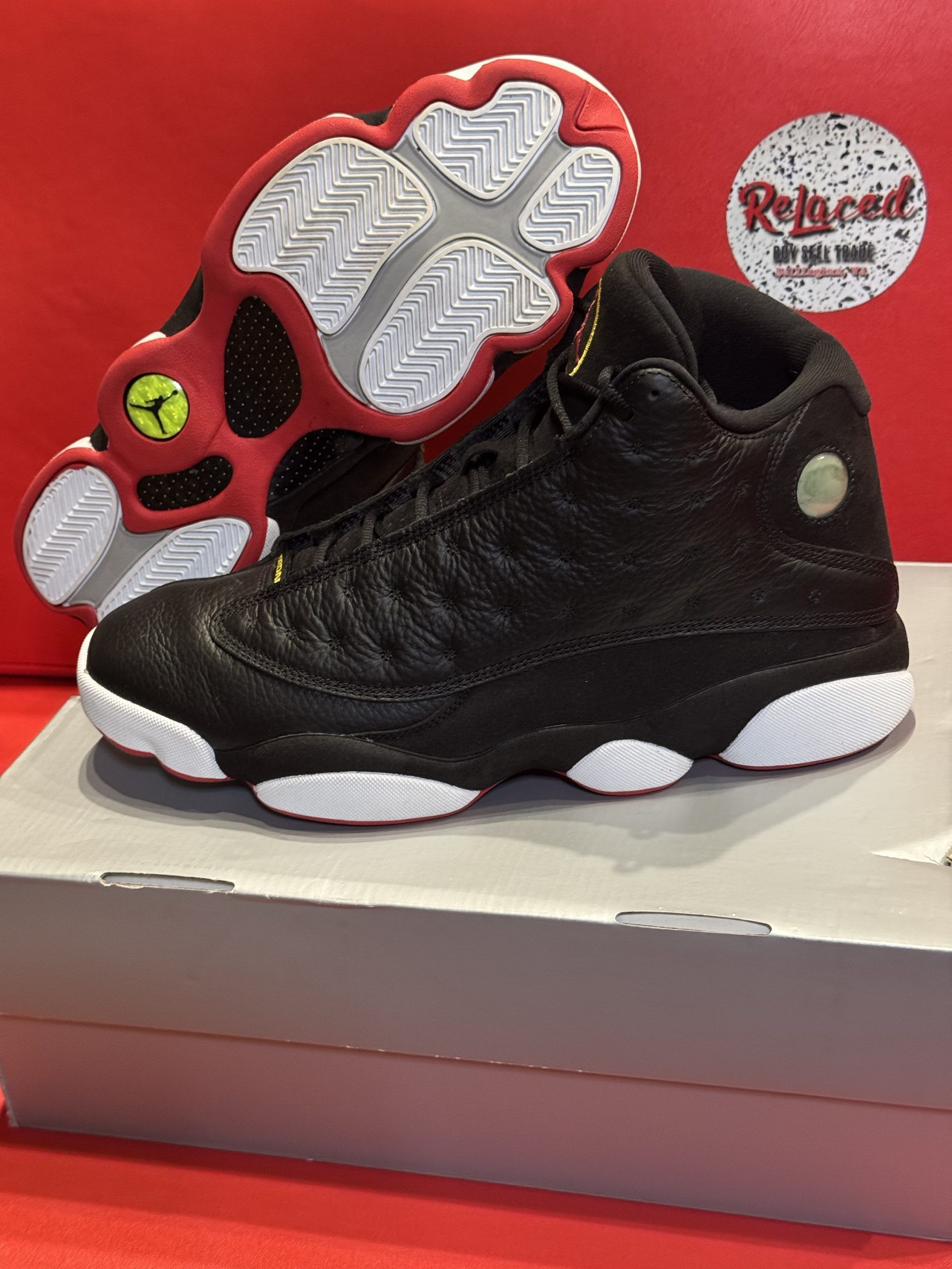 Black Air Jordan 13 sneakers with red and white accents, on a gray box.