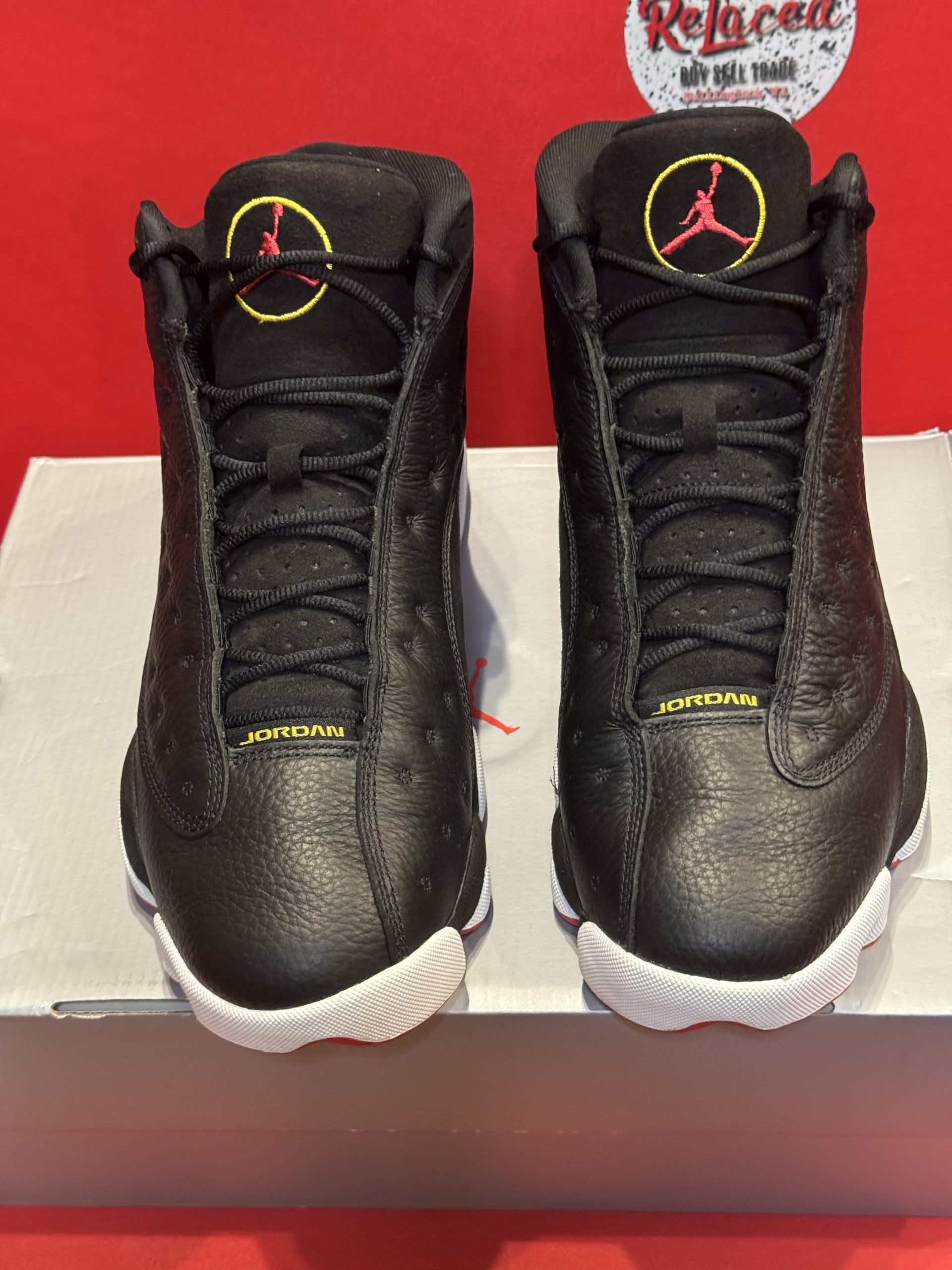 Black Air Jordan 13 sneakers with red and white accents, on a gray box.