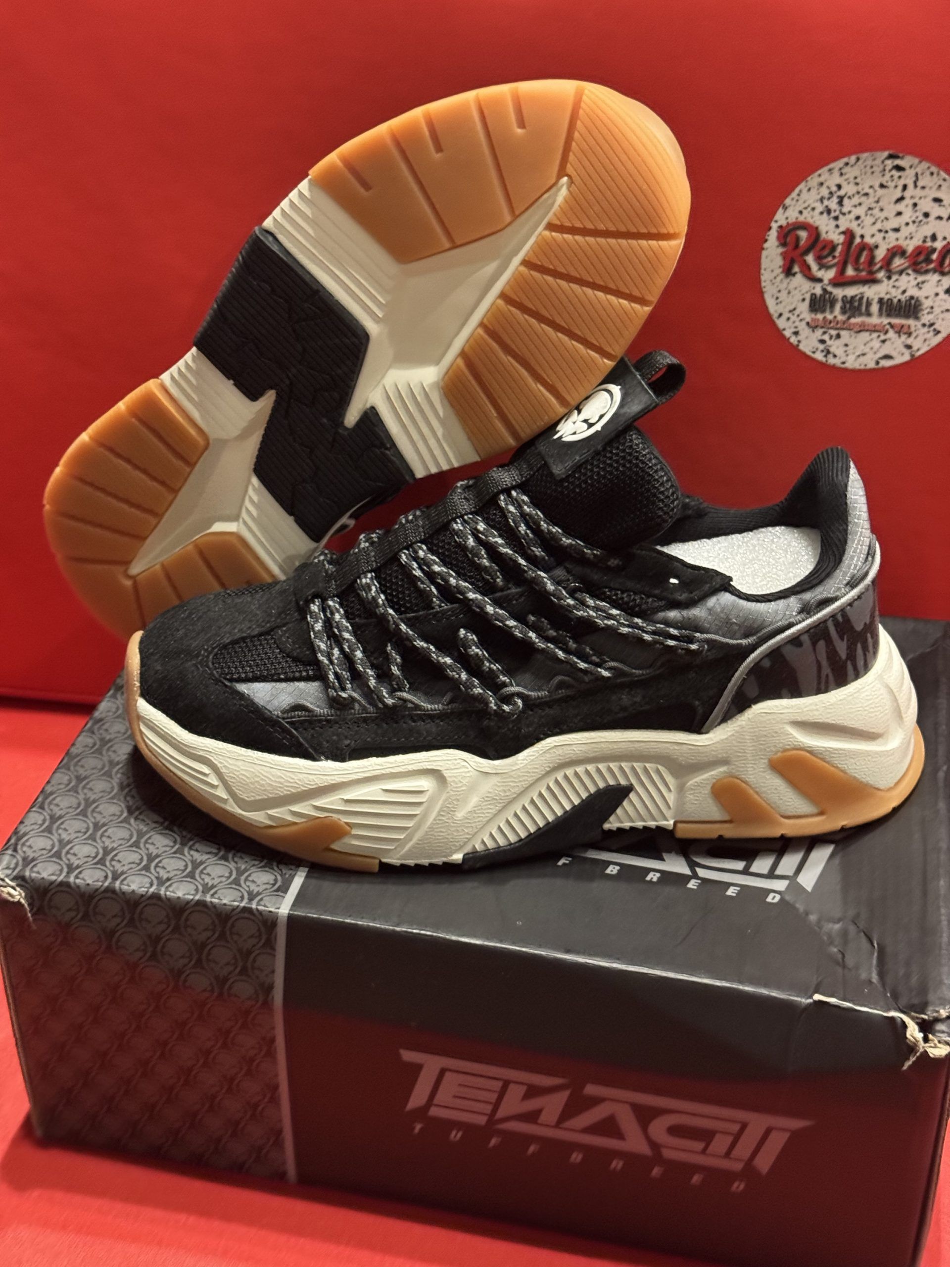 Black and white sneakers with brown soles, on top of a black box. Another shoe is shown in the background.