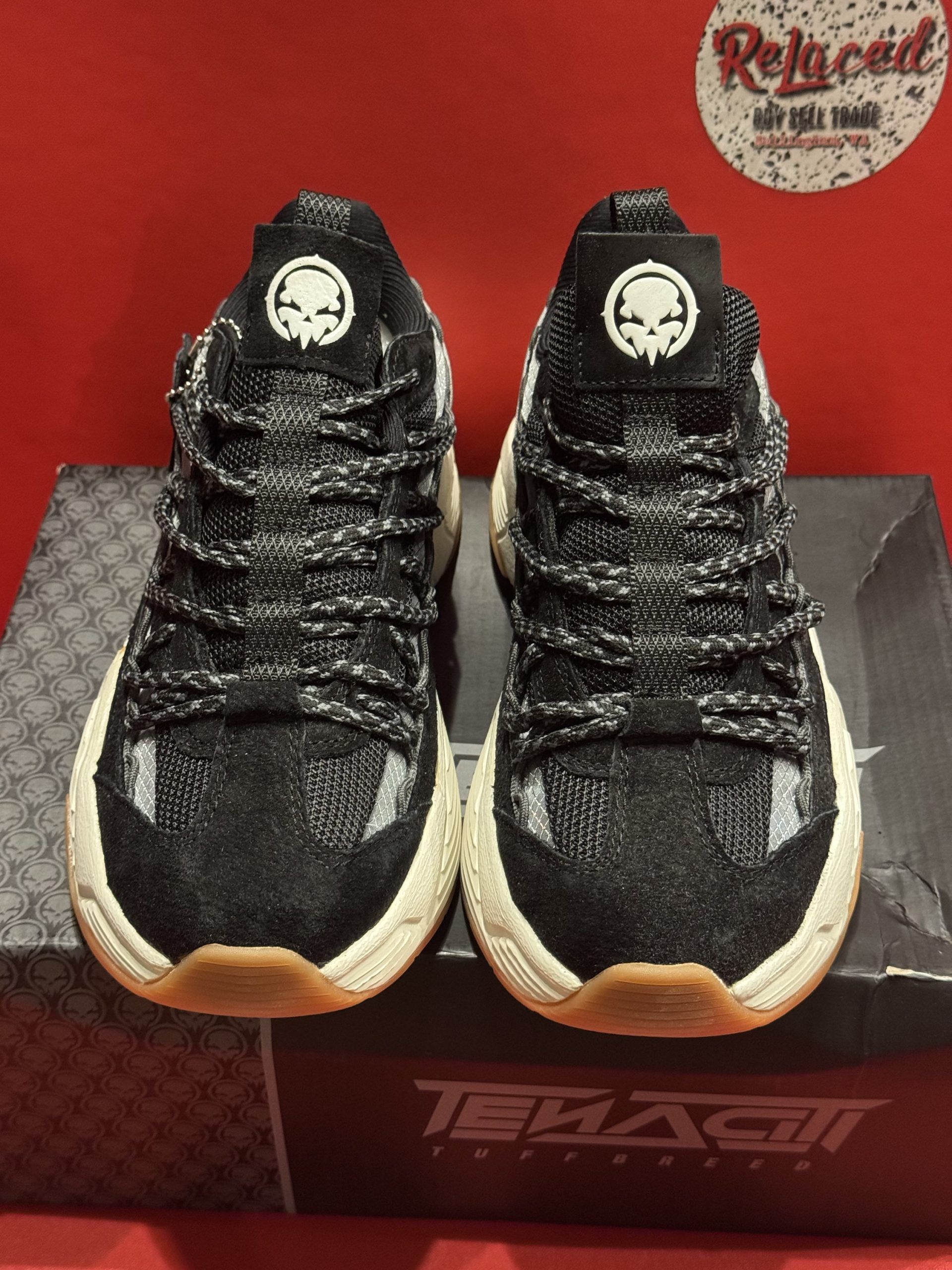 Black and white sneakers with brown soles, on top of a black box. Another shoe is shown in the background.