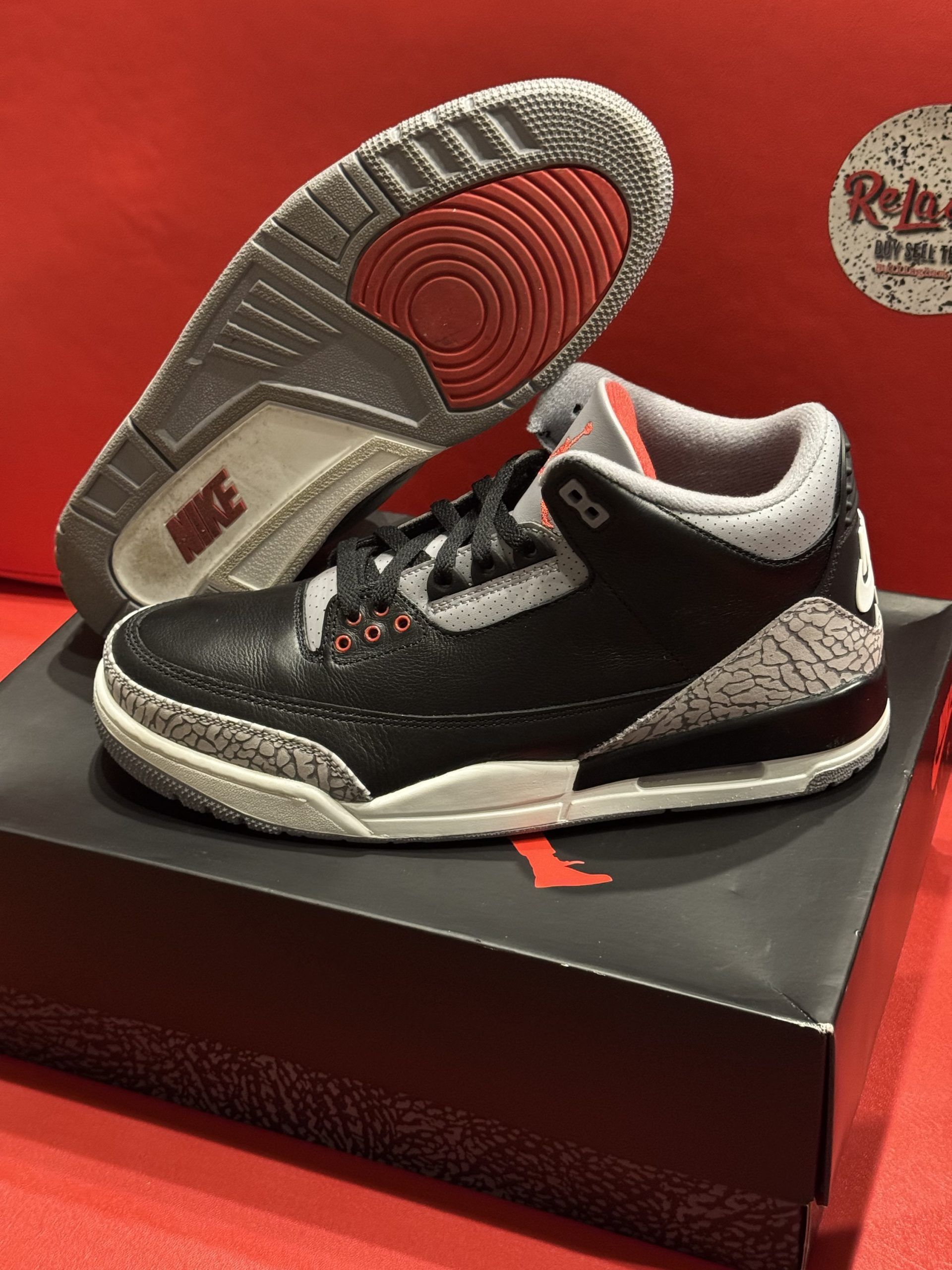 Air Jordan 3 black, grey, and red sneaker on box, sole visible.