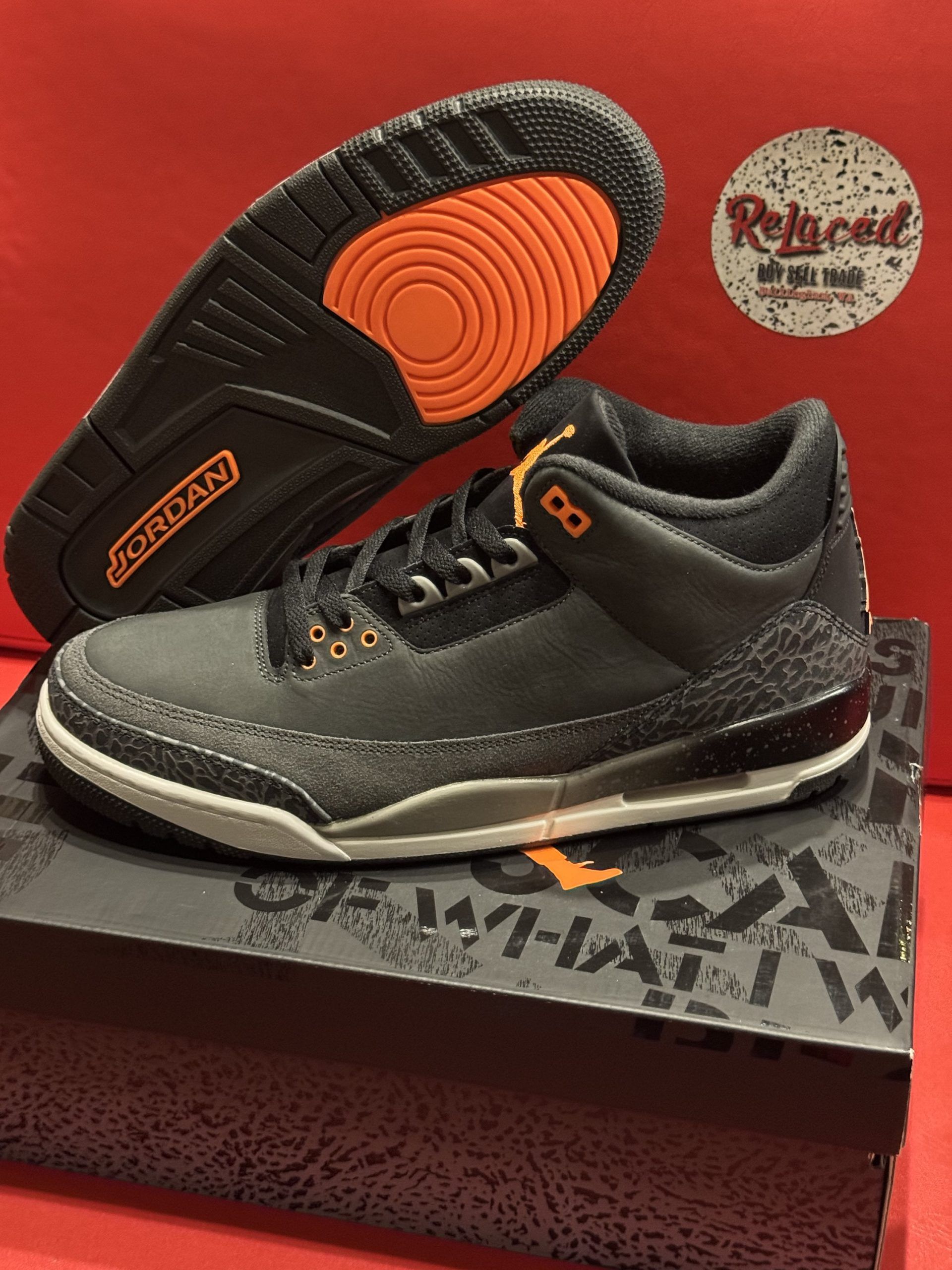Black and orange Air Jordan 3 sneakers on a patterned box. Sole is visible, featuring orange accents.