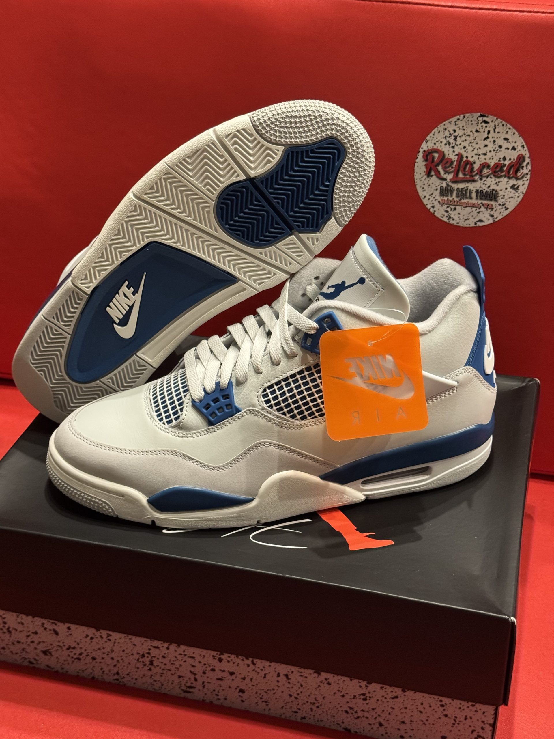 Air Jordan 4 sneakers in white and blue, displayed on a black shoebox against a red background.