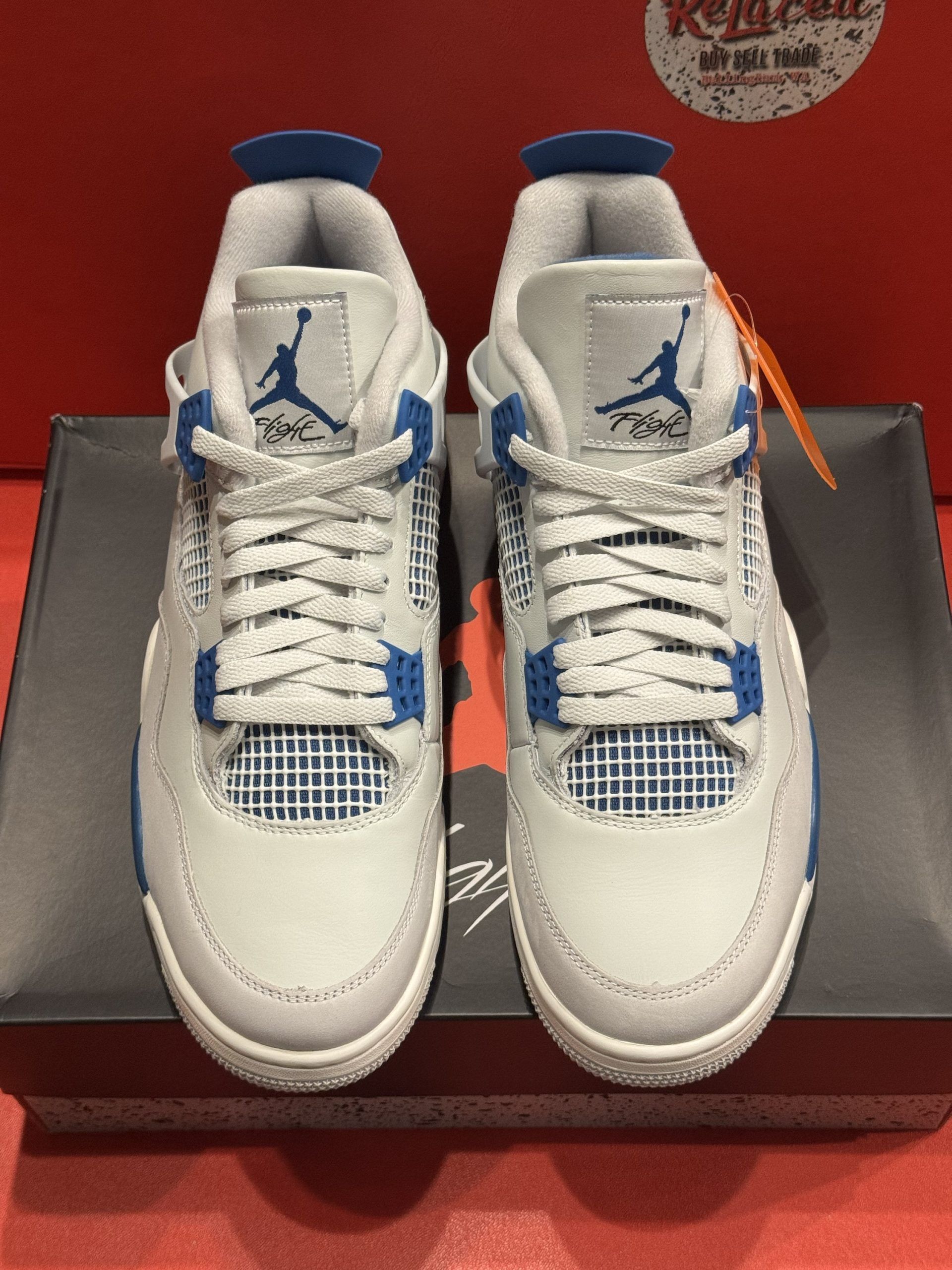 Air Jordan 4 sneakers in white and blue, displayed on a black shoebox against a red background.