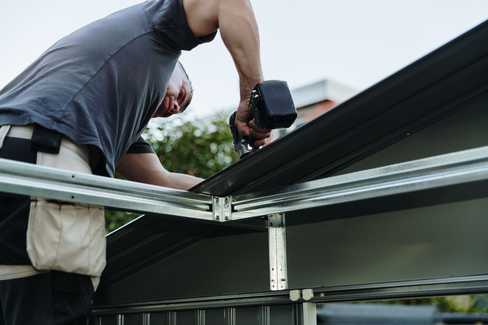 A roofer is installing roofing sheets with a drill.