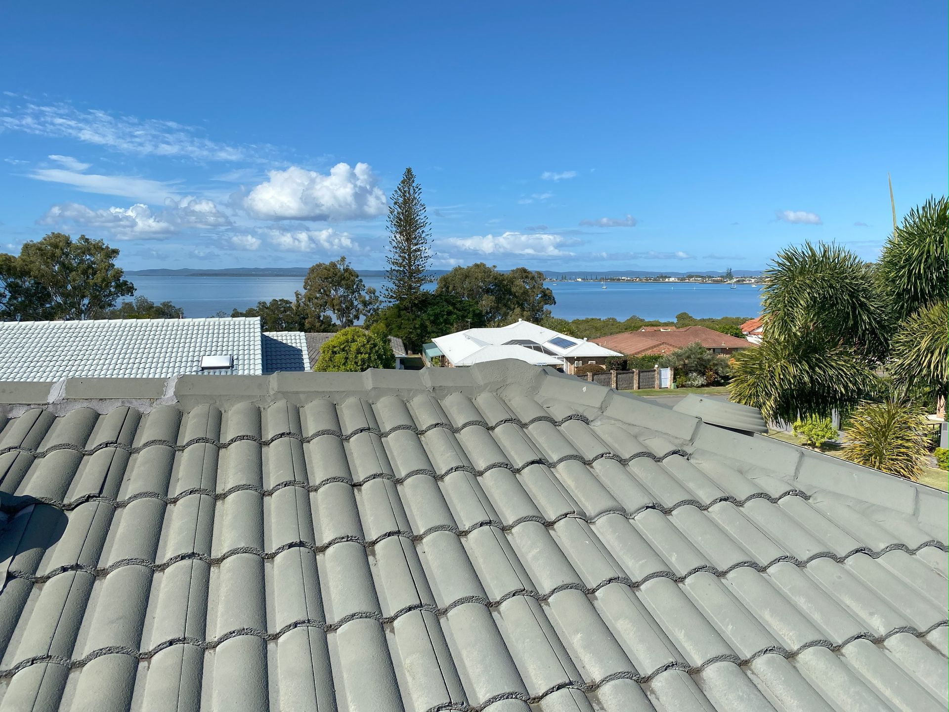 Gray tile roof with a view of the water, blue sky, and houses in the distance.