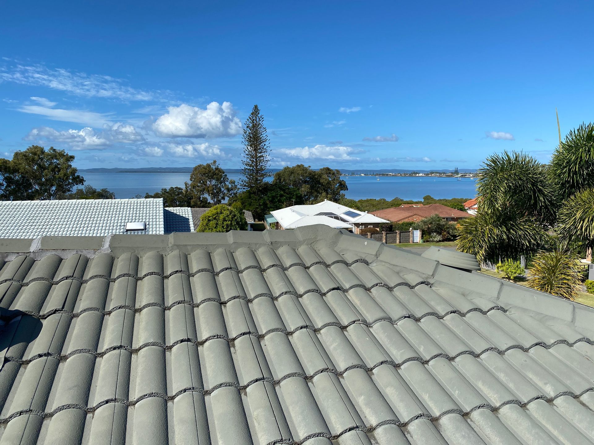 Gray tiled roof with a scenic view of water and blue sky.