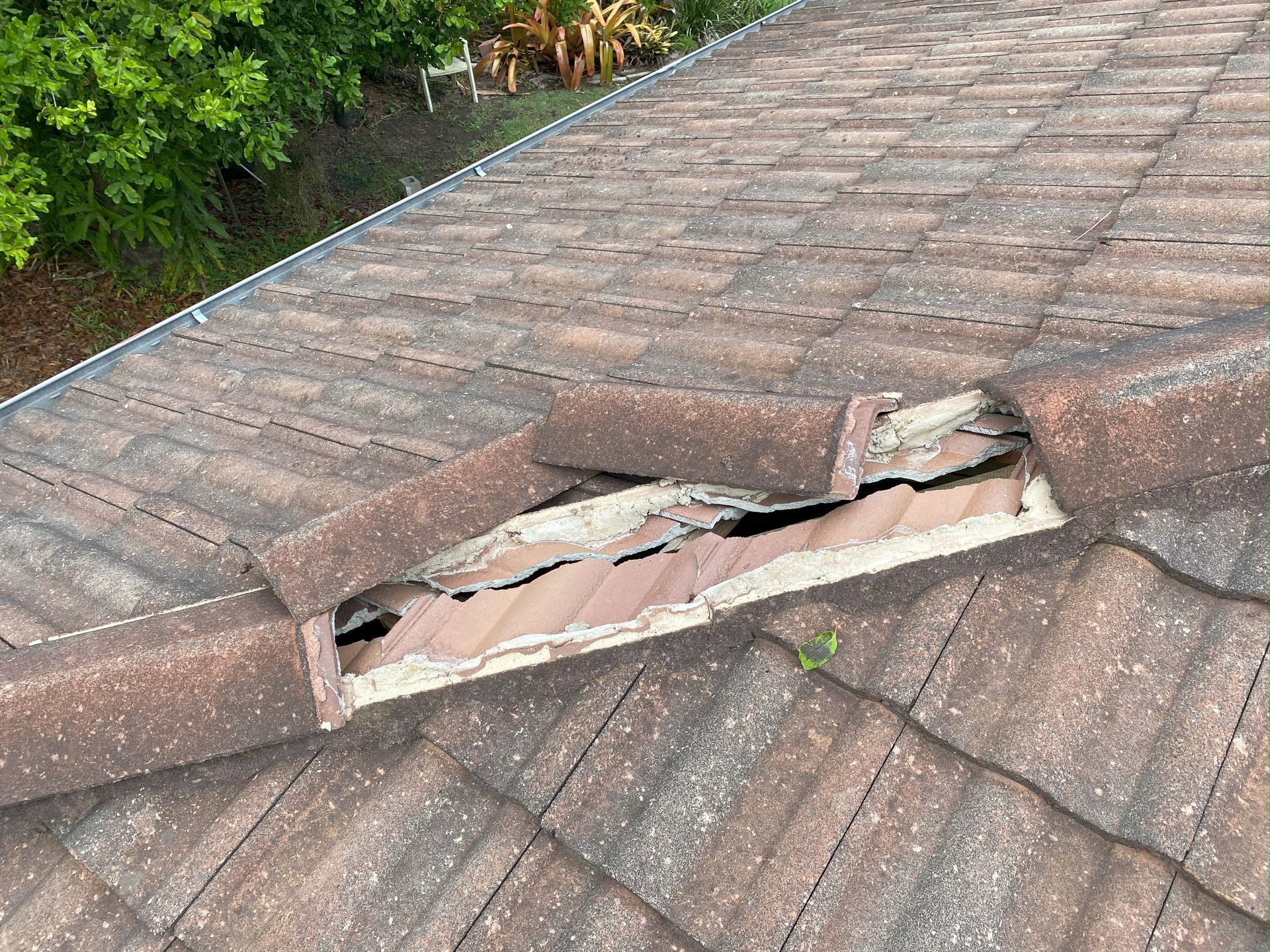 Damaged brown roof tiles with a gaping hole exposing the underlying structure.