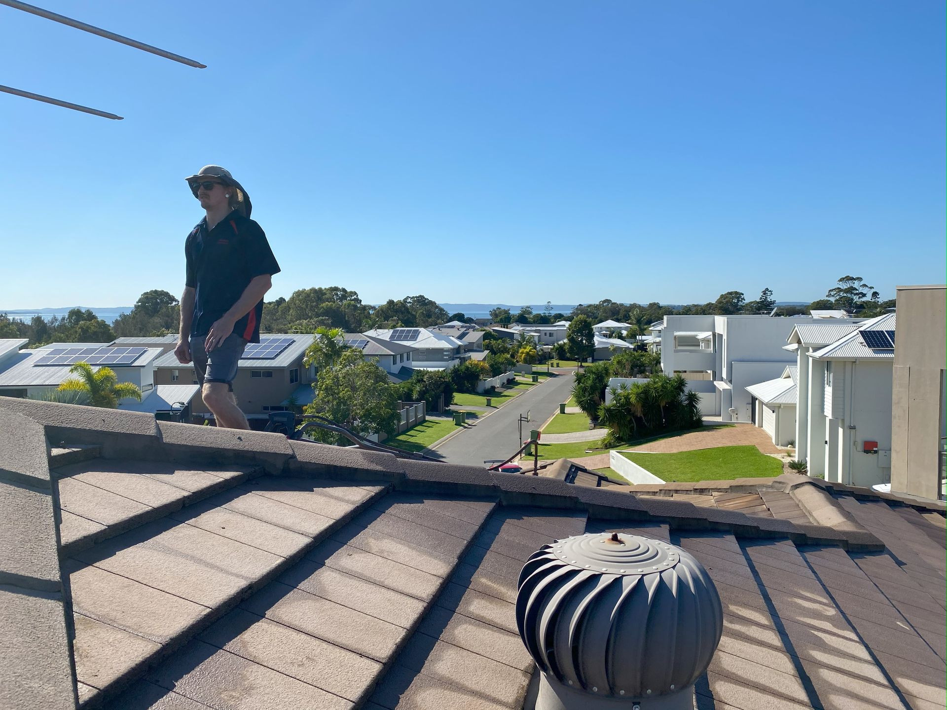 Person standing on a rooftop with a suburb and ocean view on a sunny day.