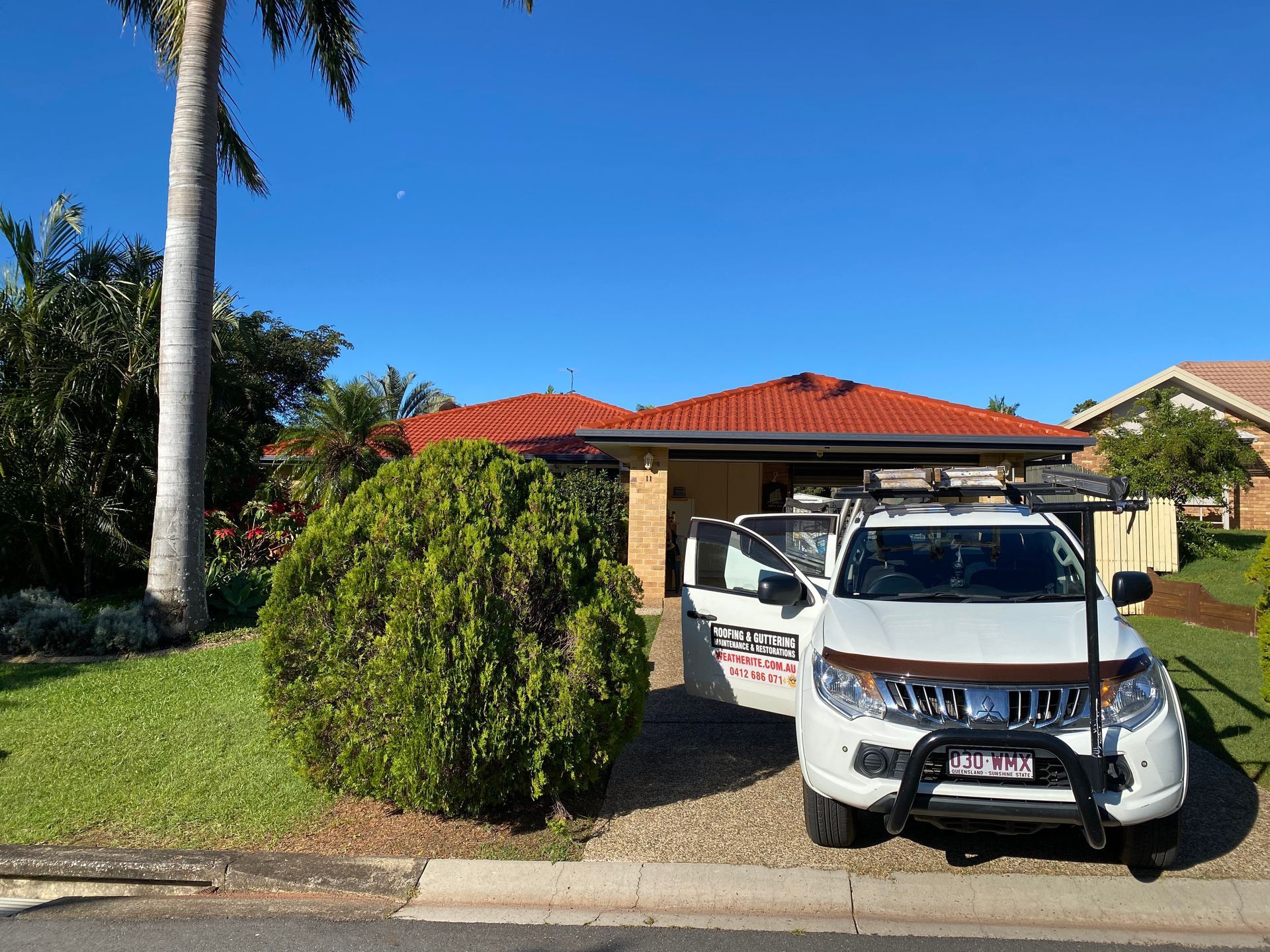 White service truck parked in front of a home; bush and palm tree in yard.