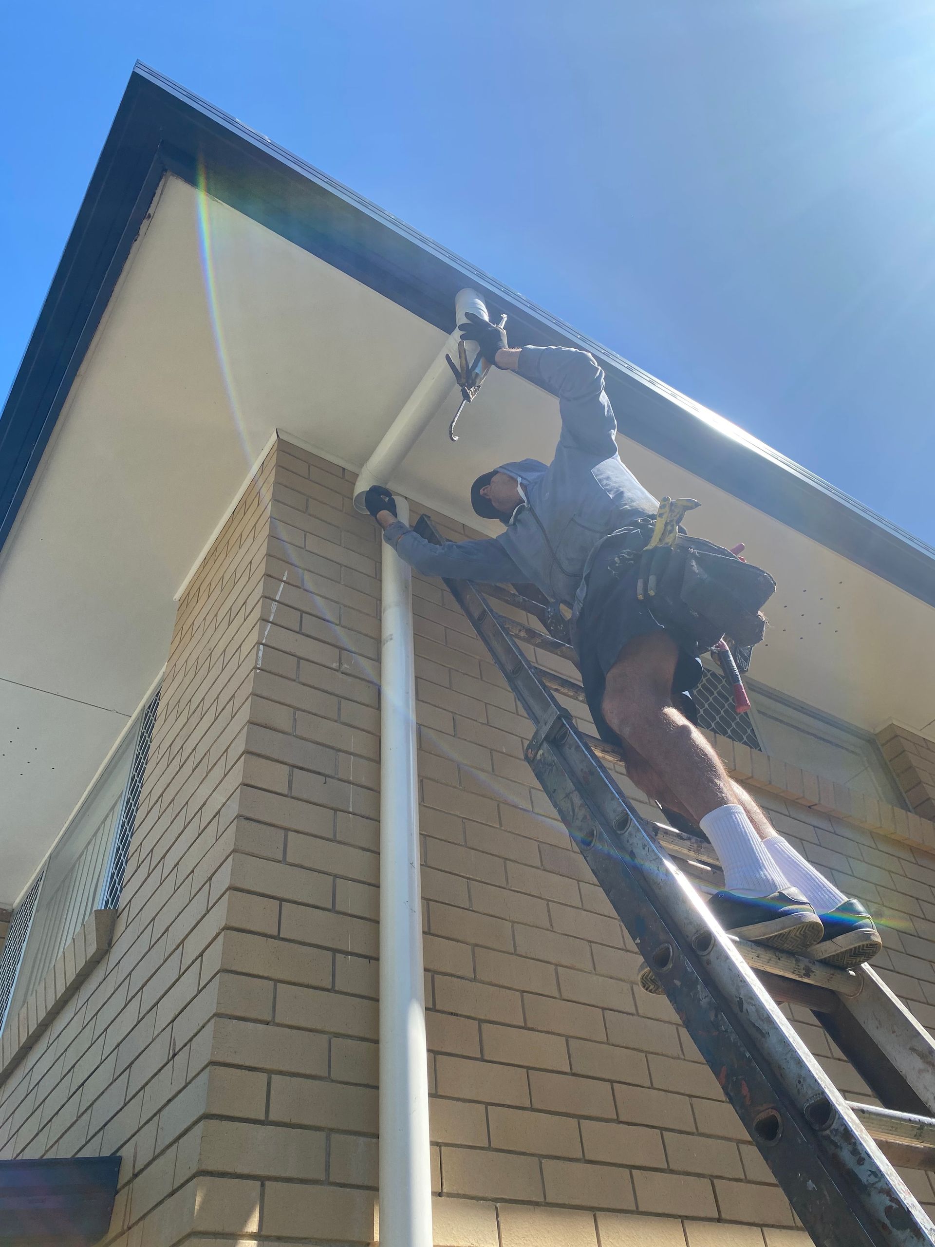 Man on ladder installing gutter on a brick house, sunny day.