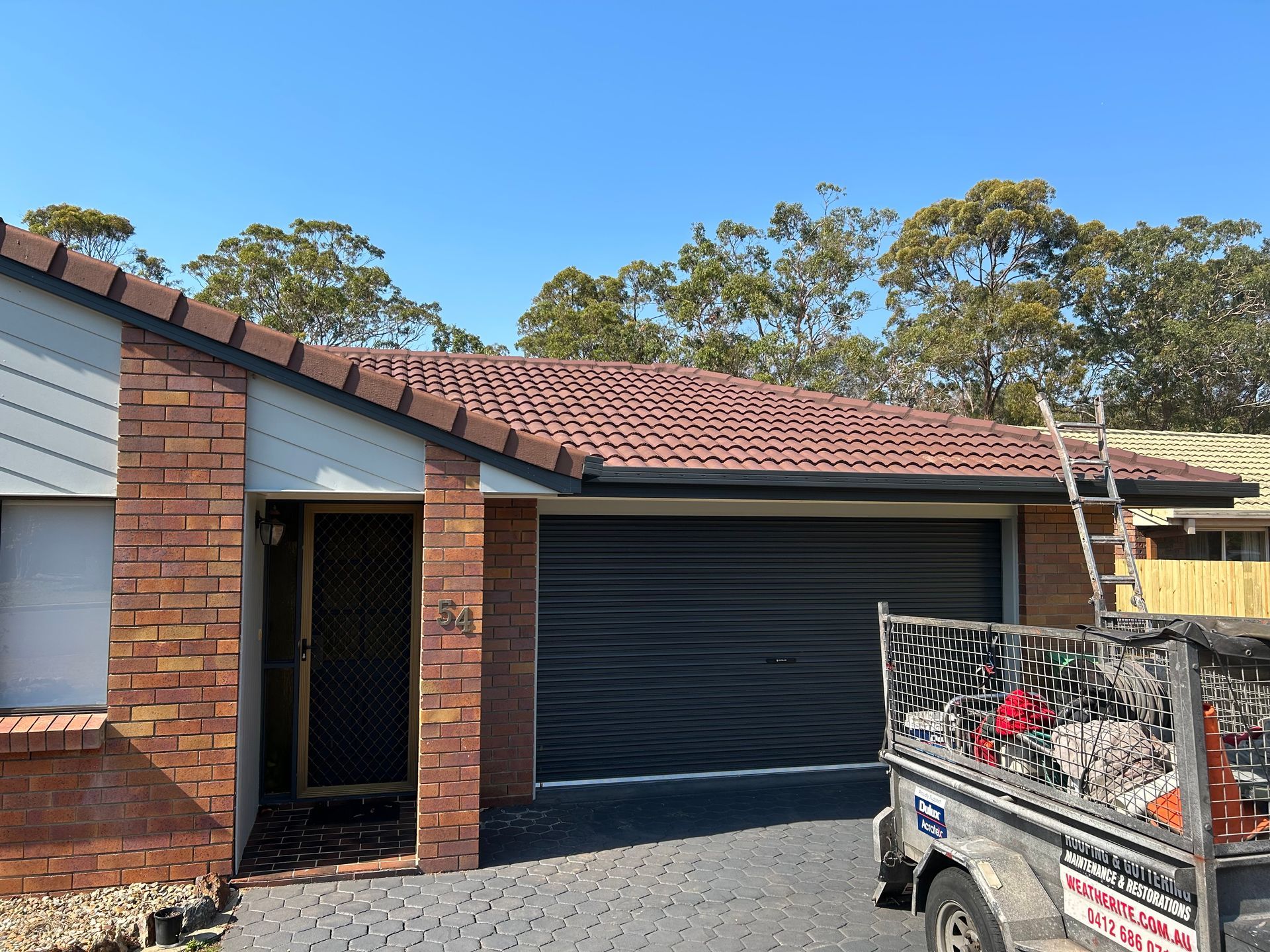 House with brown roof, garage door, brick facade, and a trailer with tools.