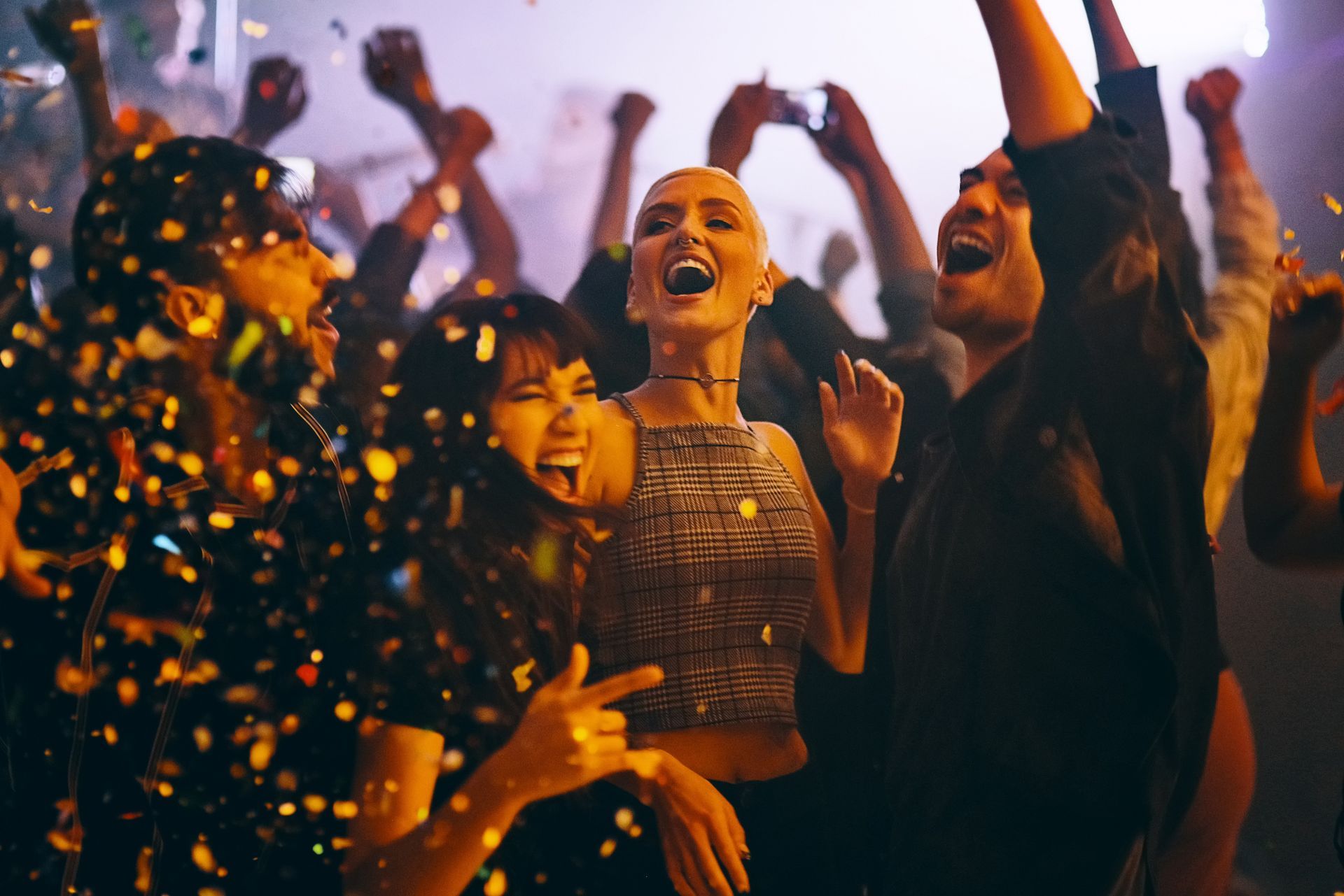 A group of people are dancing in a club with confetti falling from the ceiling.