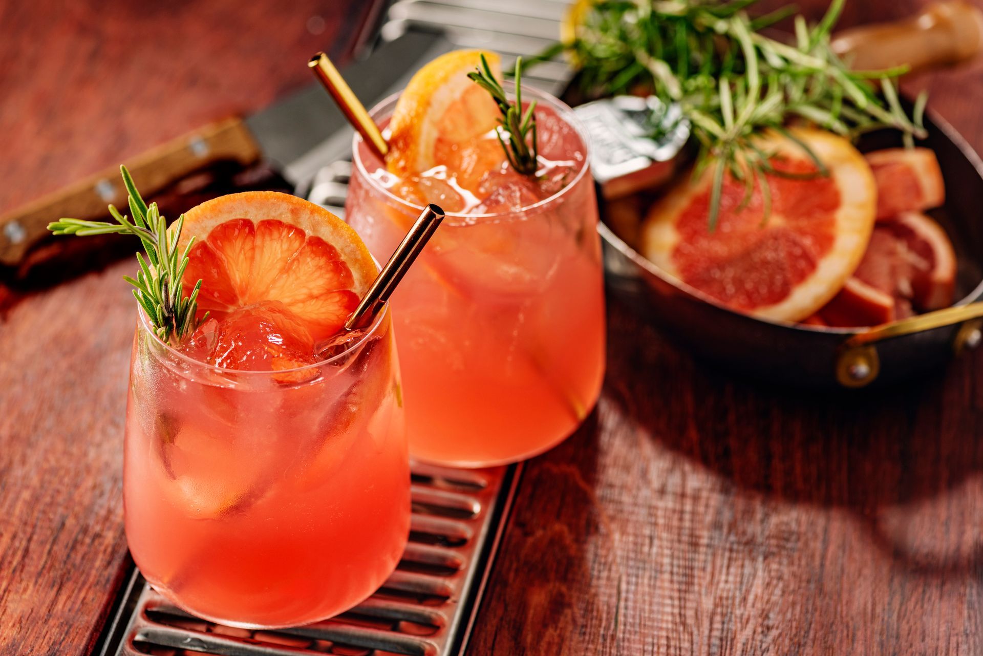 Two glasses of grapefruit juice with straws on a wooden table.
