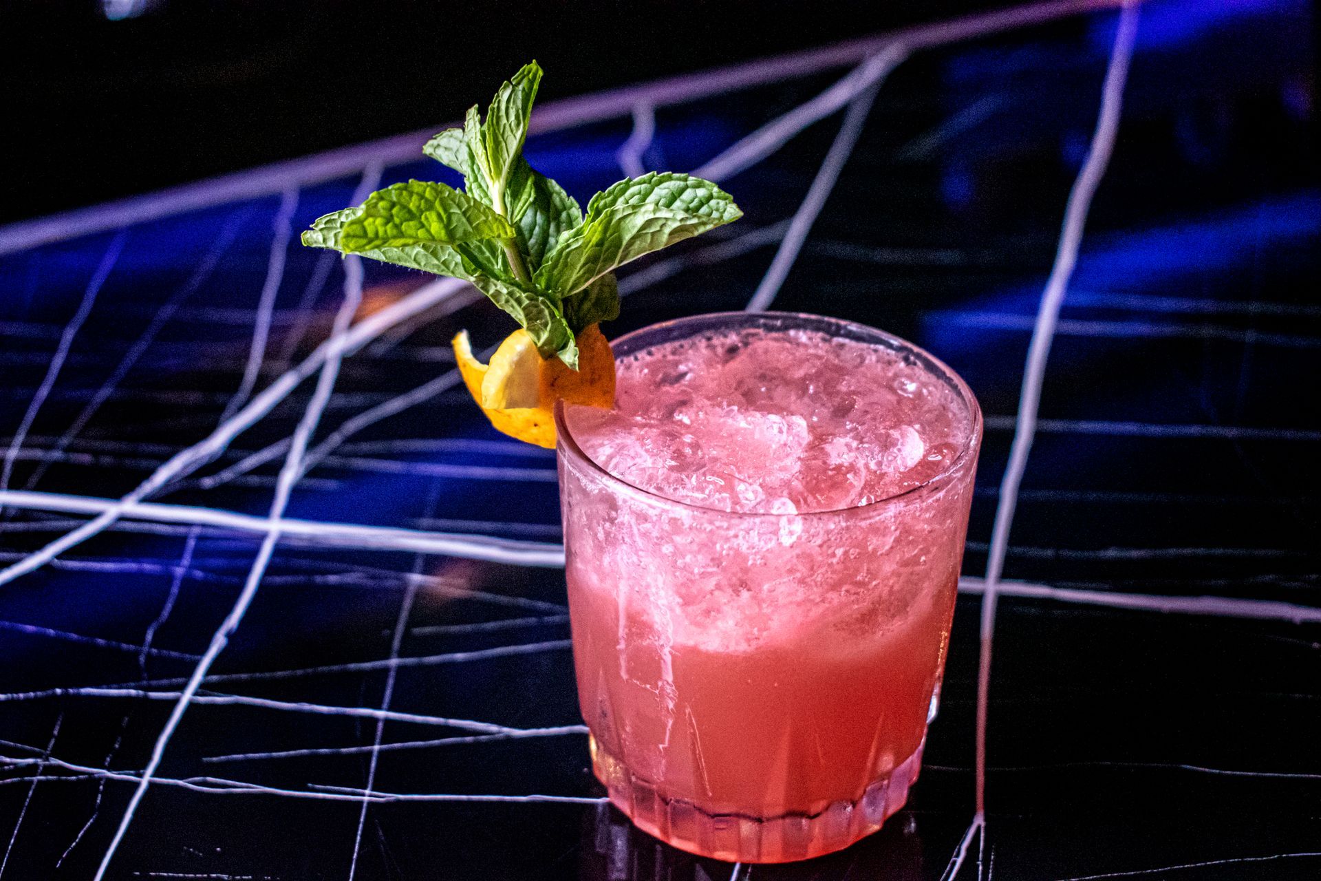 A close up of a pink cocktail with ice and mint on a table.