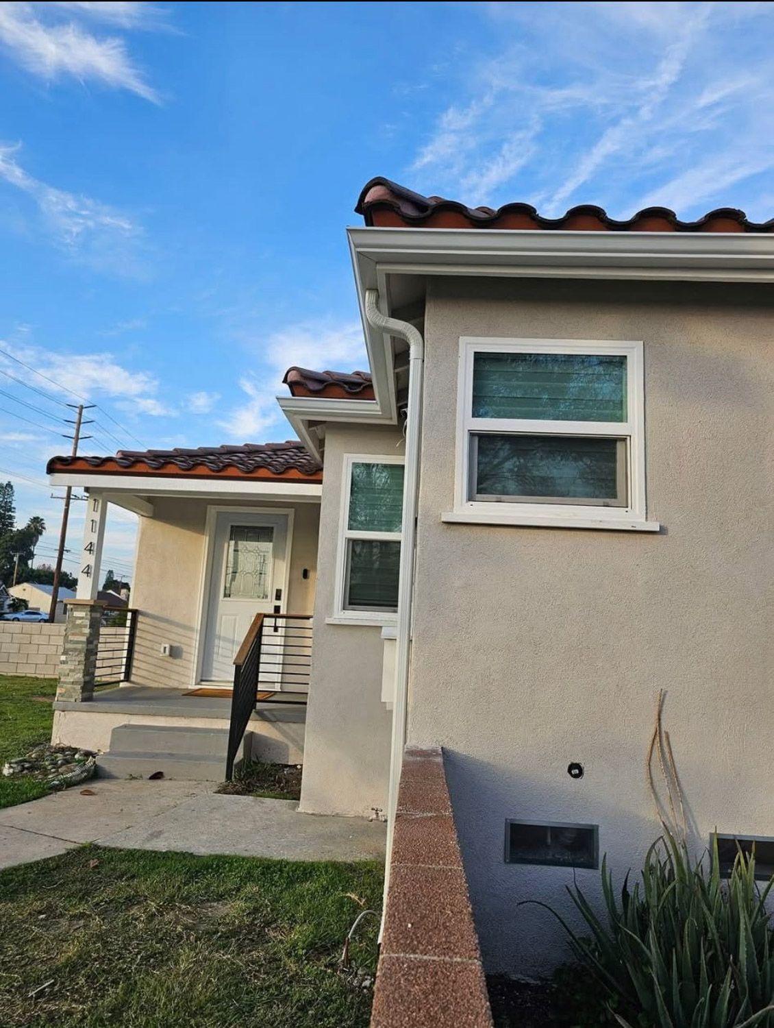 White house with black trim, a brick chimney, and landscaping under a blue sky. New seamless gutters installed by Gutter Specialist in Reno, NV