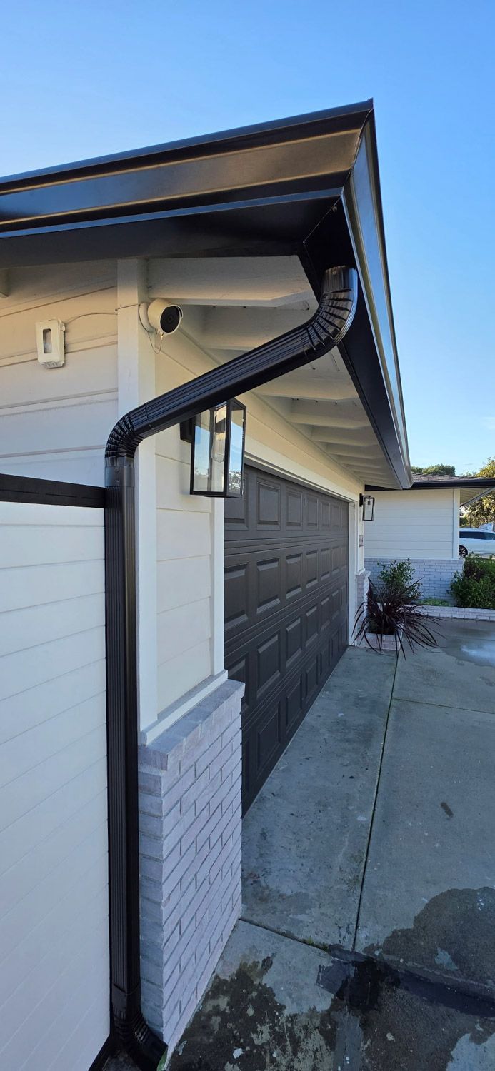Black gutter on a white and gray brick house with a dark garage door.