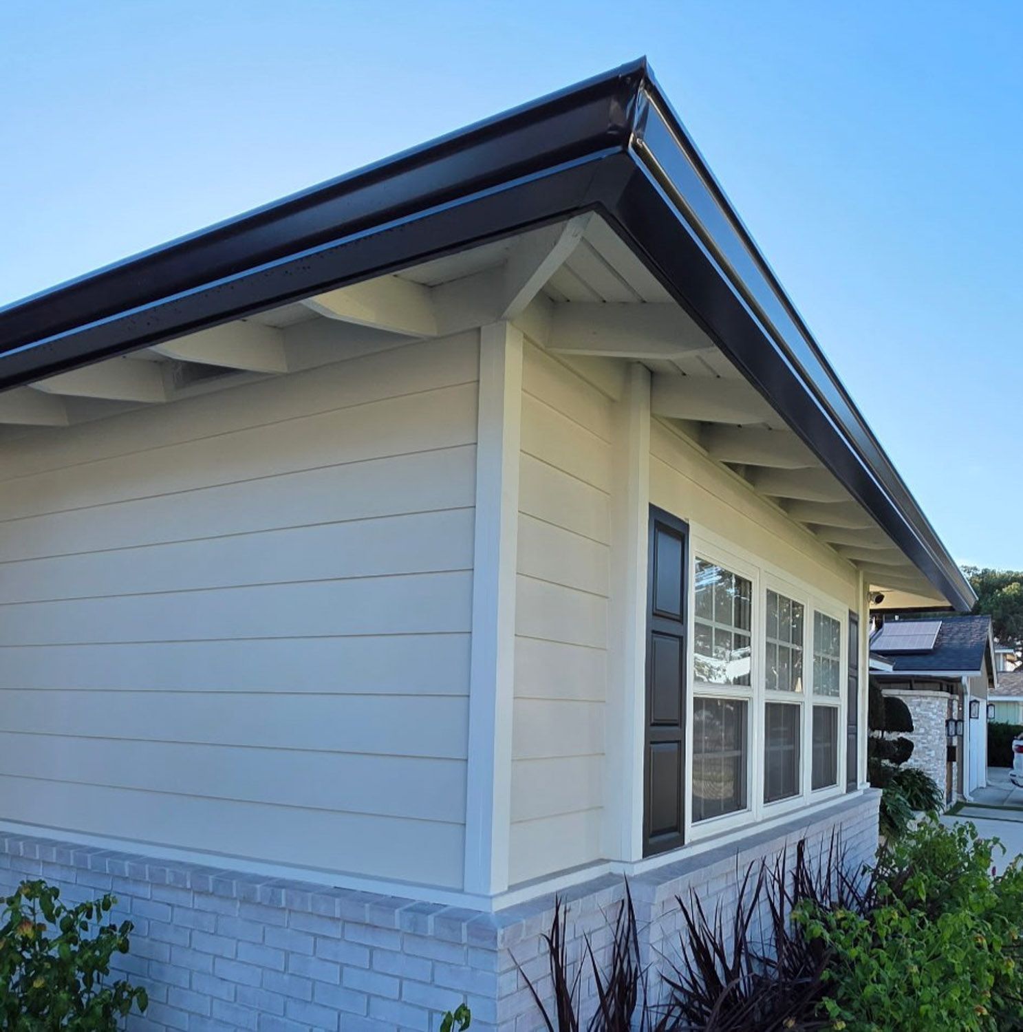 White house with black trim, a brick chimney, and landscaping under a blue, Reno, NV sky. New Seamless gutters installed by Gutter Spcialist.