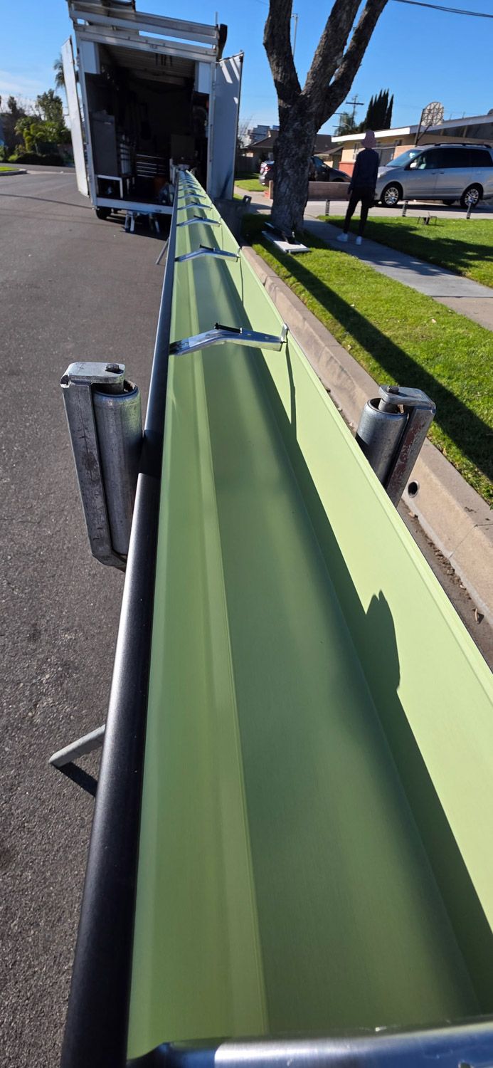 Long green gutter being loaded from a truck on a street, likely for installation. New seamless gutters installed by Gutter Specialist in Reno, NV
