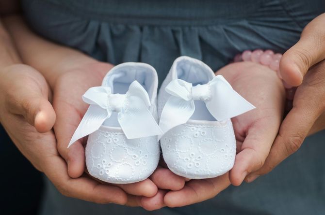 A couple is holding a pair of baby shoes in their hands.