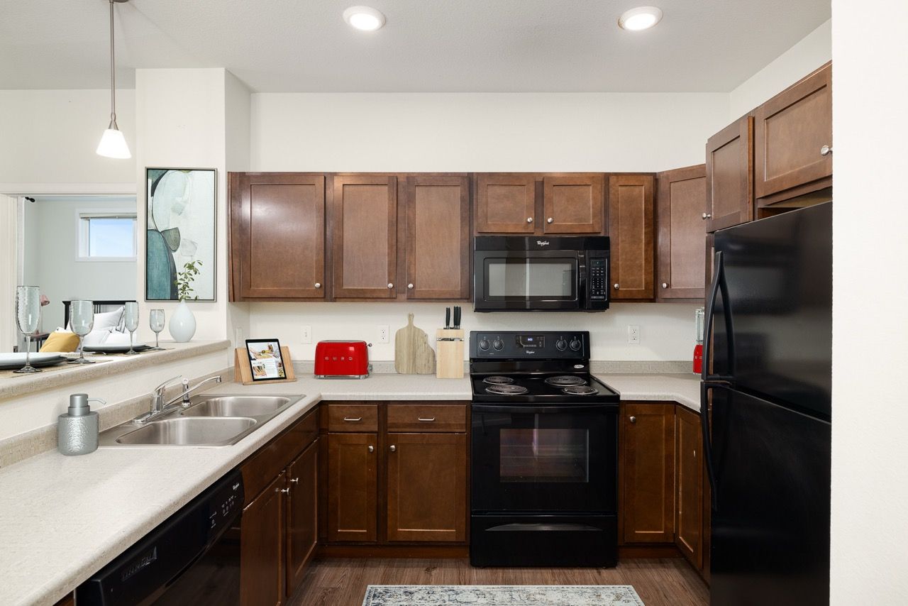 U-shaped kitchen with dark wood cabinets, black appliances, and a double stainless steel sink.