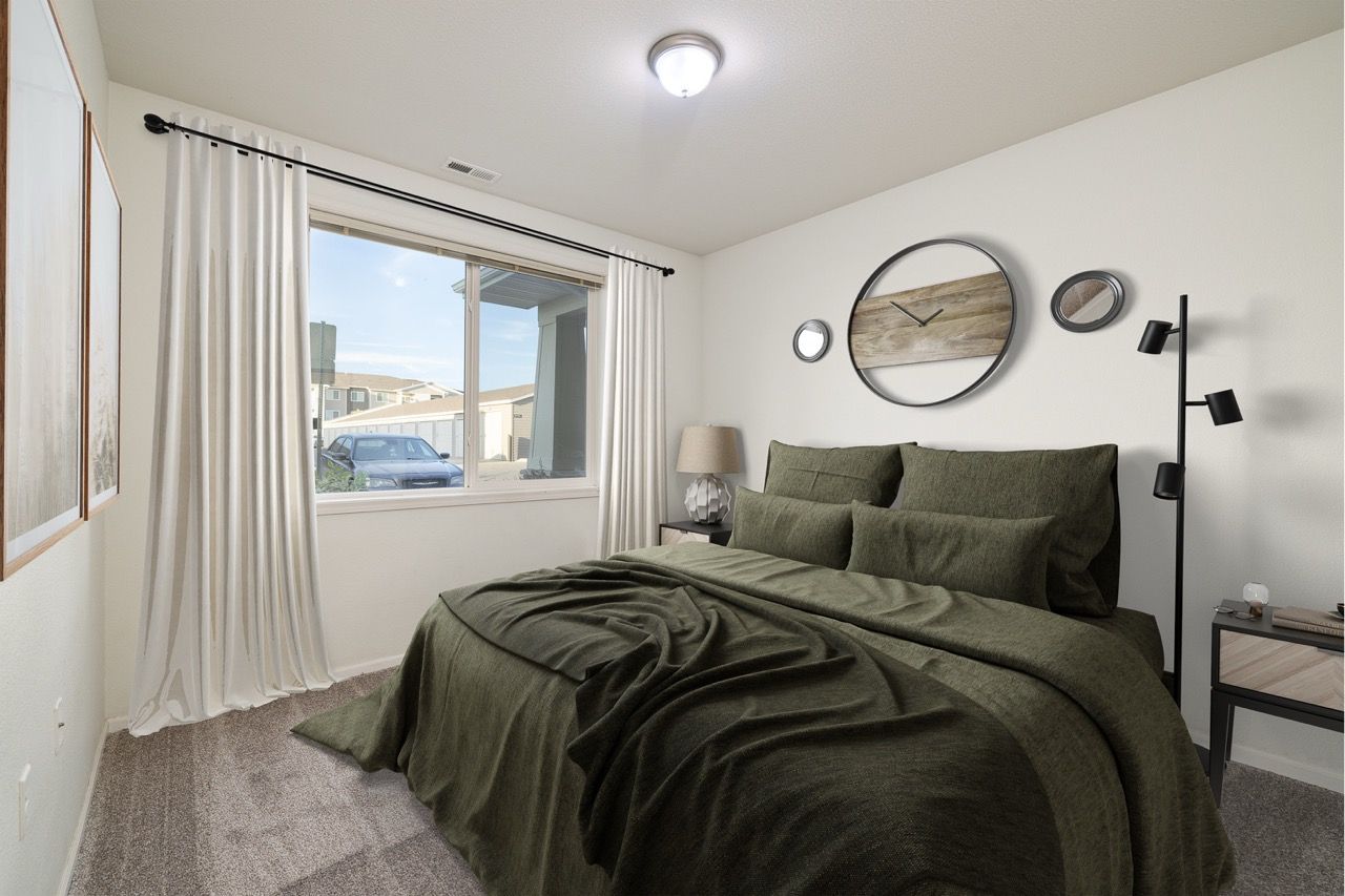 Bedroom in an apartment with a bed, green bedding, nightstand, and window with white curtains.