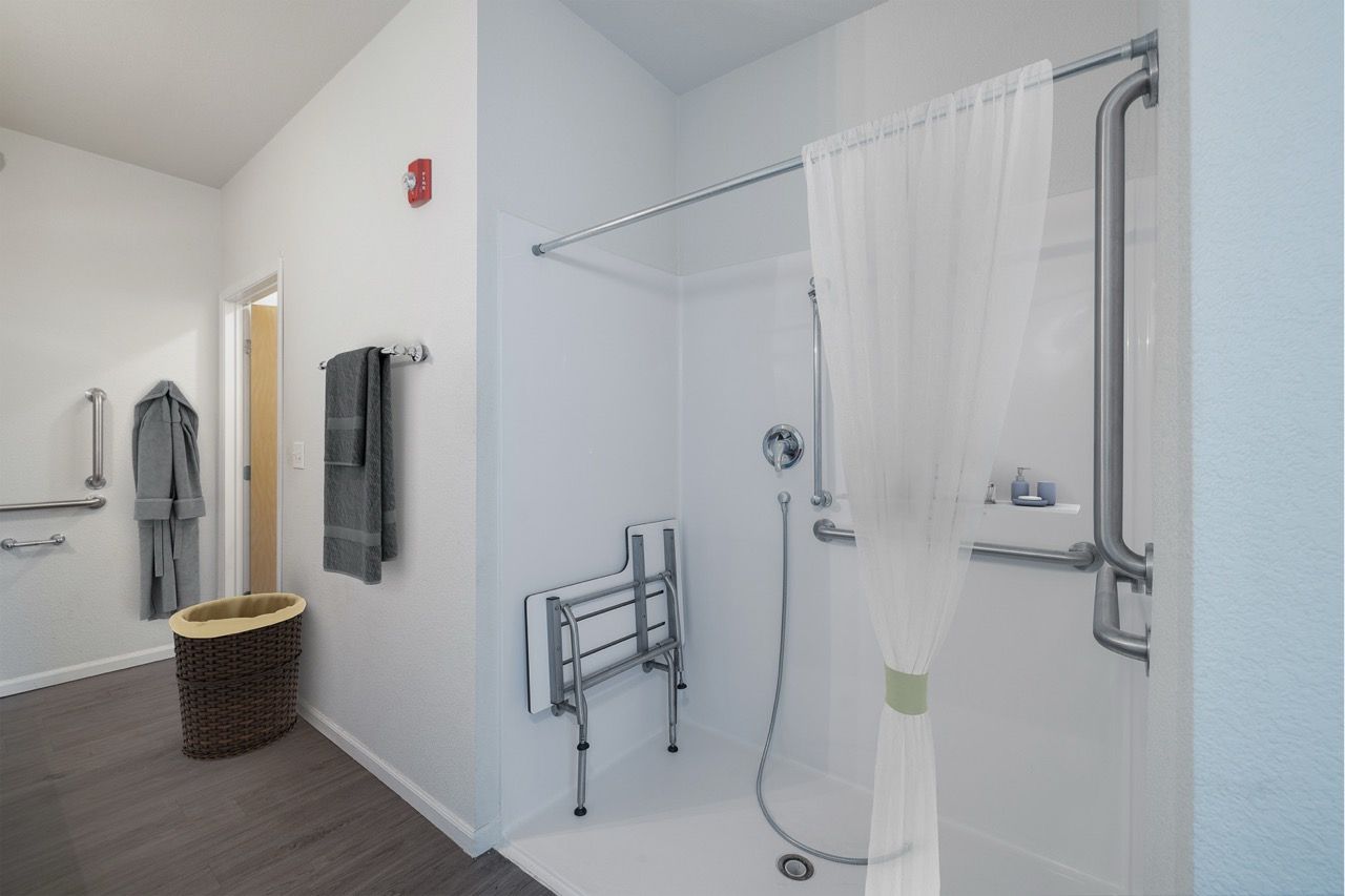 Accessible apartment bathroom shower with grab bars and a curtain.