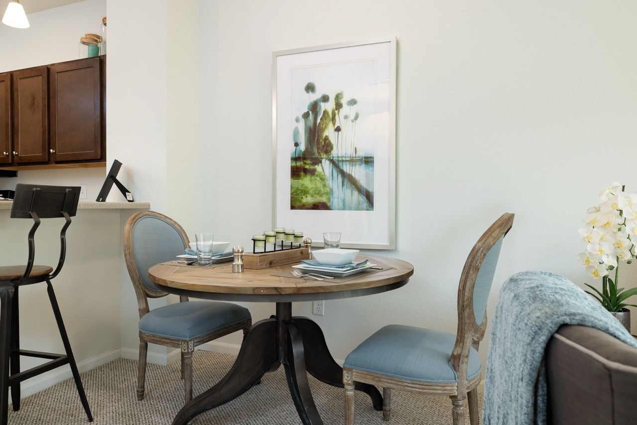 Dining nook with round wooden table, two blue-upholstered chairs, and wall art in a modern apartment.