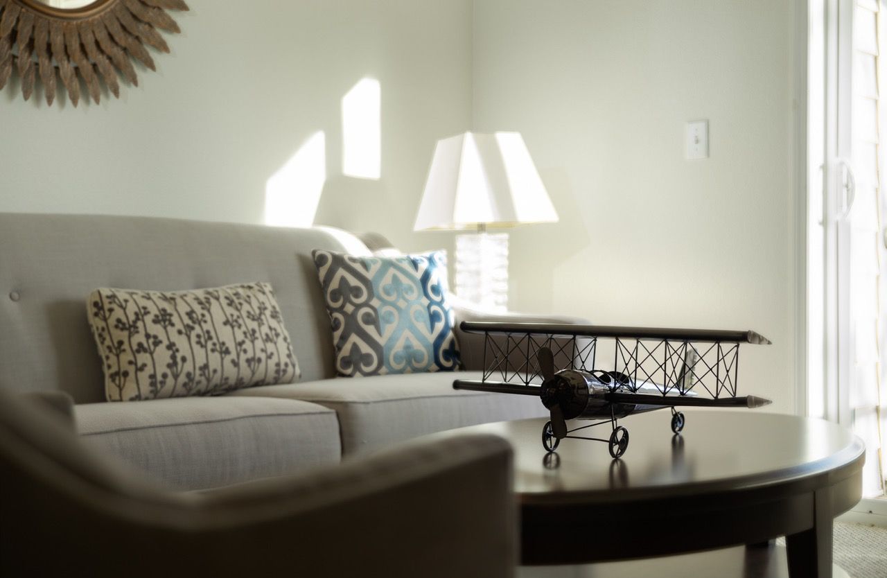 Living room with beige sofa, decorative pillows, a lamp, and a model airplane on a round coffee table.