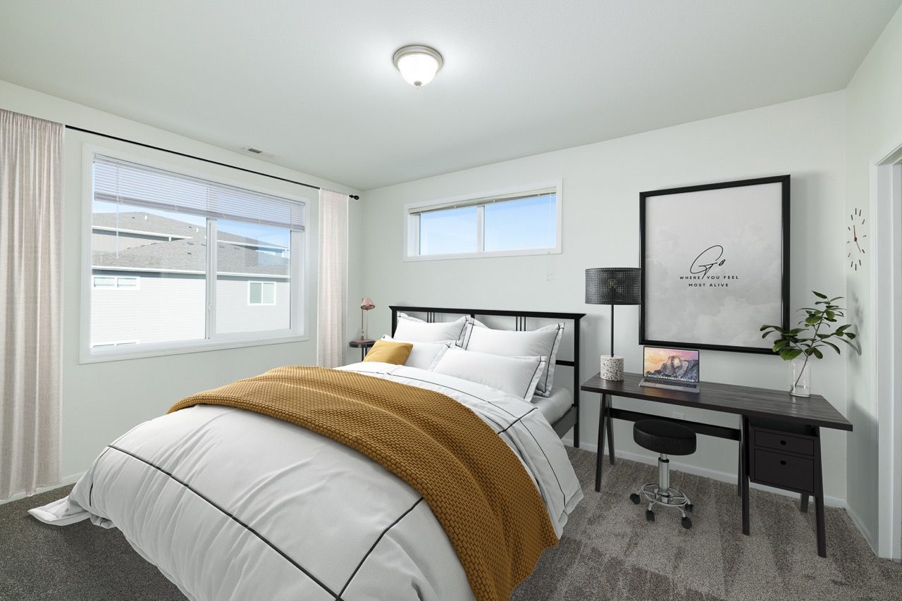 Bedroom in an apartment with a made bed, desk, lamp, wall art, and a window with blinds.