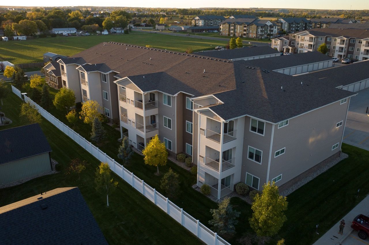 Aerial view of a multi-story apartment building with balconies, a white fence, and manicured lawns.
