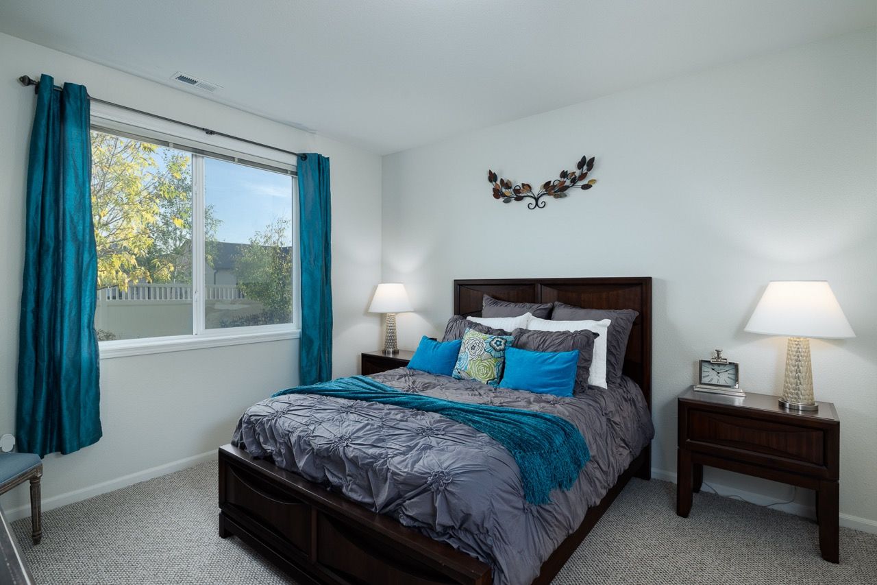 Bedroom with dark wood bed, gray bedding, two nightstands, and blue curtains.