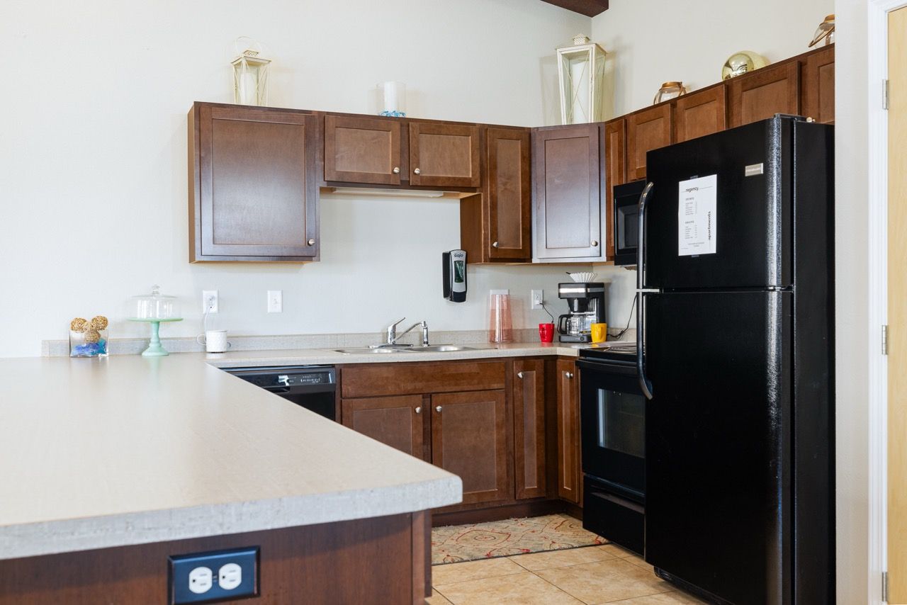 Apartment kitchen with dark wood cabinets, beige countertops, and a black refrigerator.