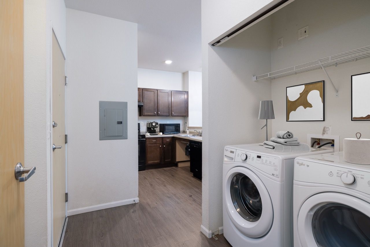 Laundry area with a front-load washer and a dryer next to a small kitchen.