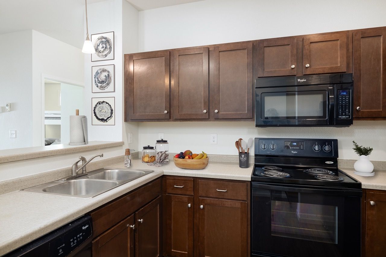 Kitchen with dark wood cabinets, beige countertops, a double sink, and a black stove with microwave above.