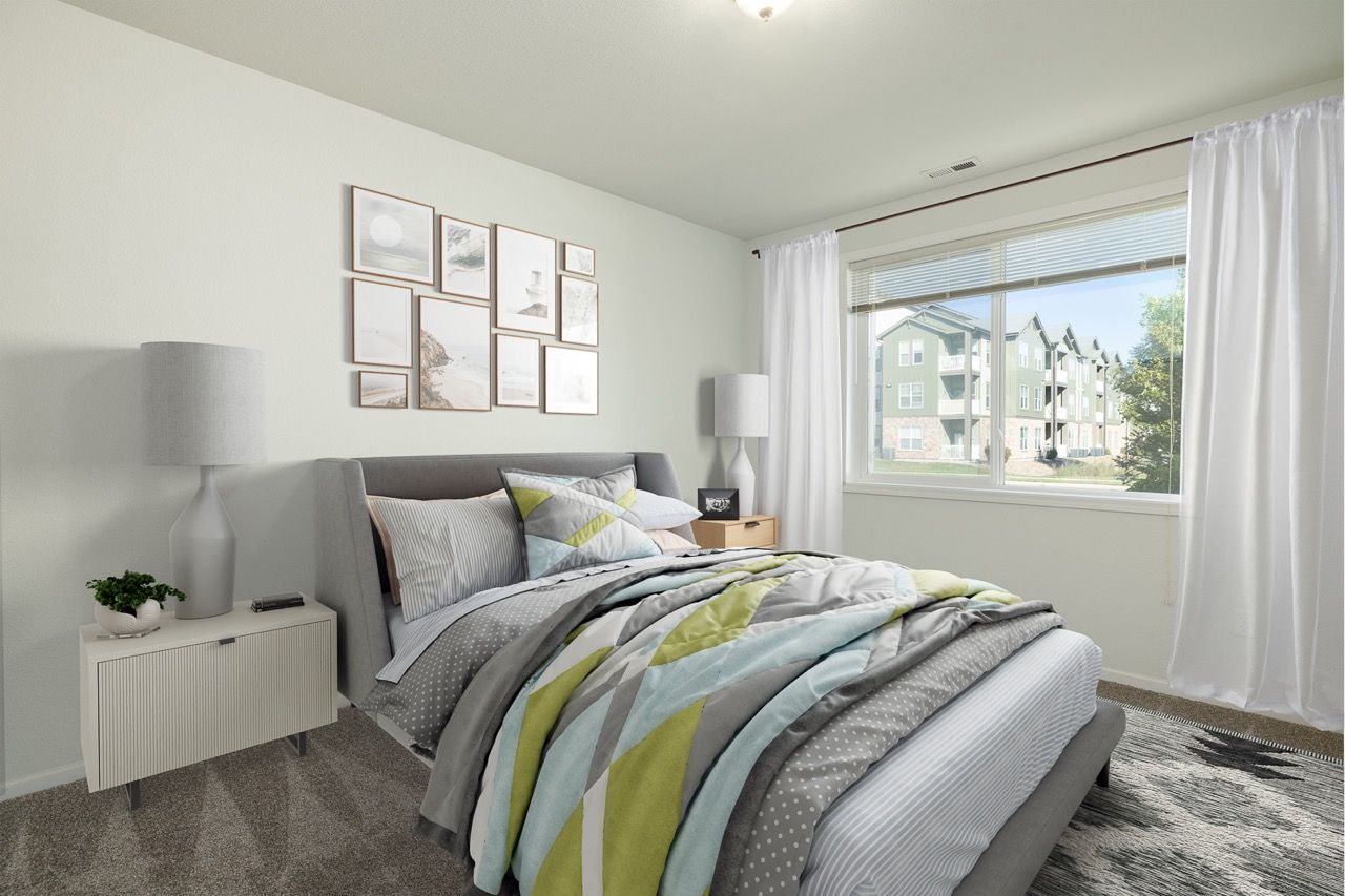Bedroom in an apartment with a gray upholstered bed, nightstands, and a large window with white curtains.