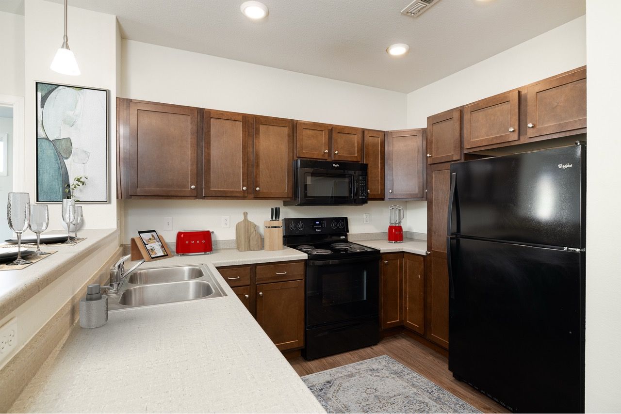 U-shaped kitchen with dark wood cabinets, white countertops, double sink, and black appliances.