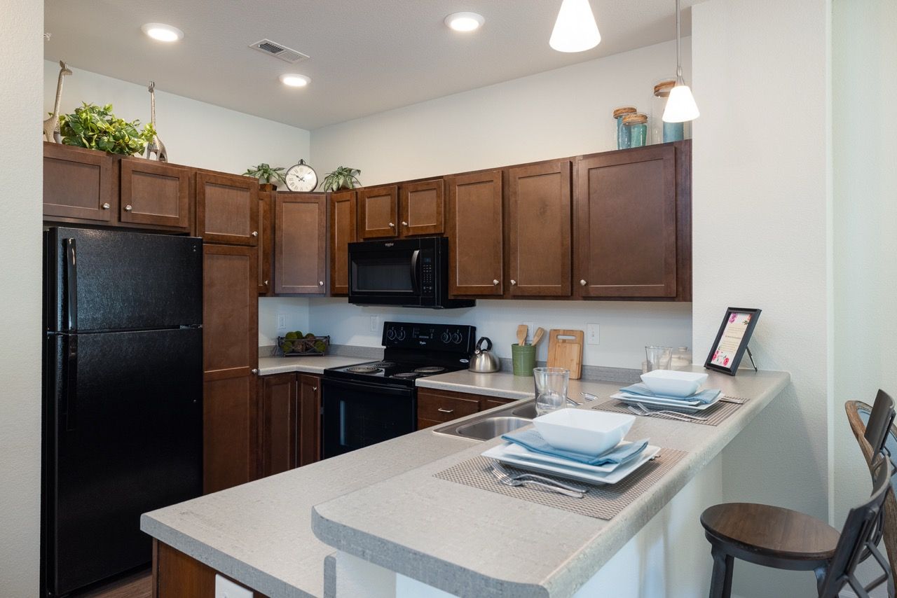 Kitchen in an apartment with dark wood cabinets, black refrigerator, microwave, and a breakfast bar.