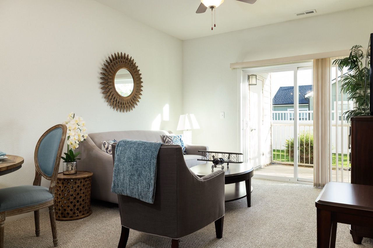 Living room in an apartment with a beige sofa, blue chair, coffee table, and sliding glass doors to a balcony.