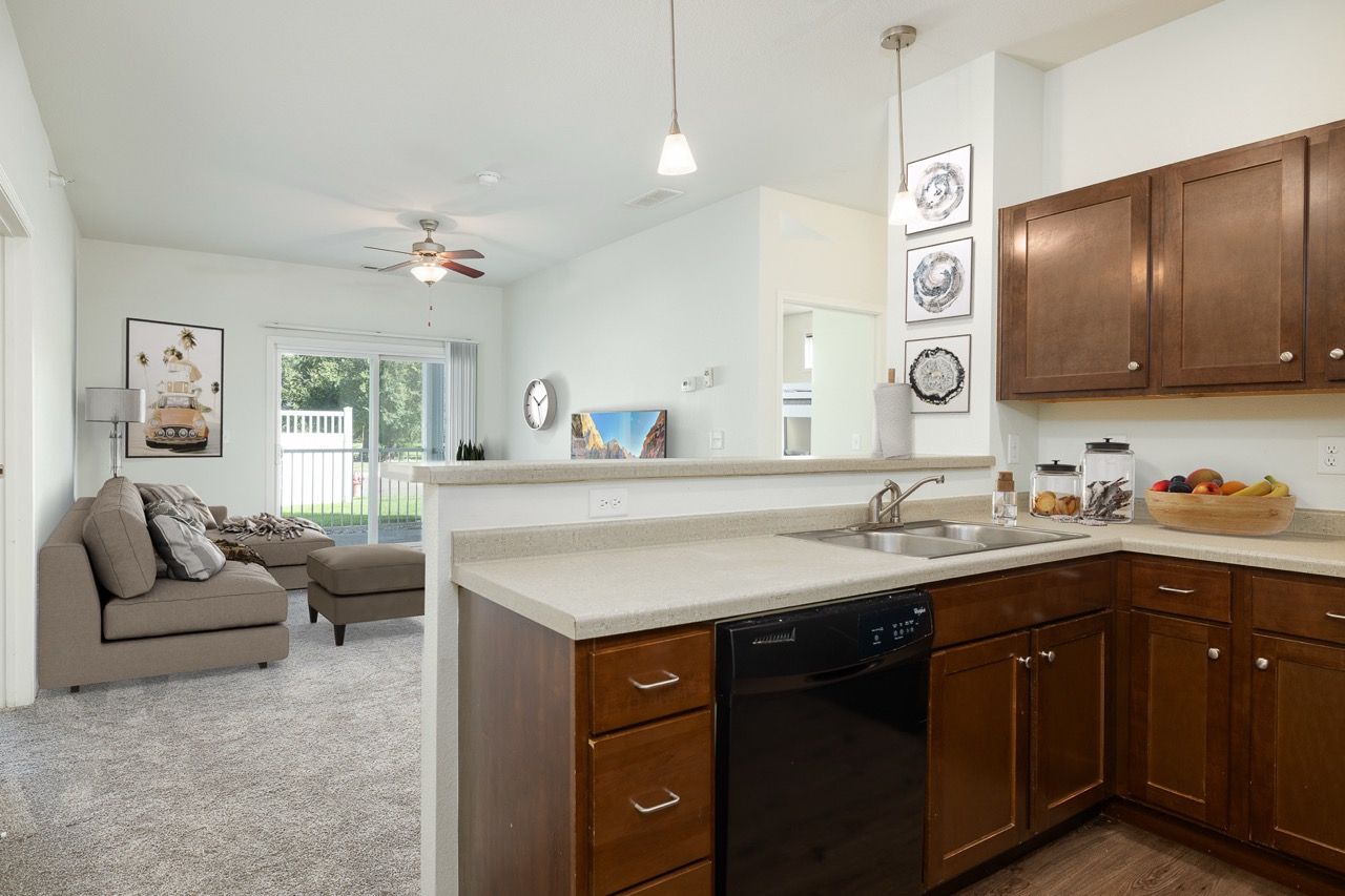 Open-concept kitchen with dark wood cabinets, beige countertops, and a living area in view.