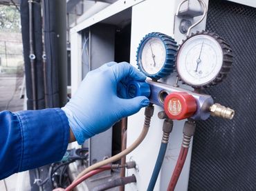 A person wearing blue gloves uses a HVAC manifold gauge set to service an air conditioning unit.