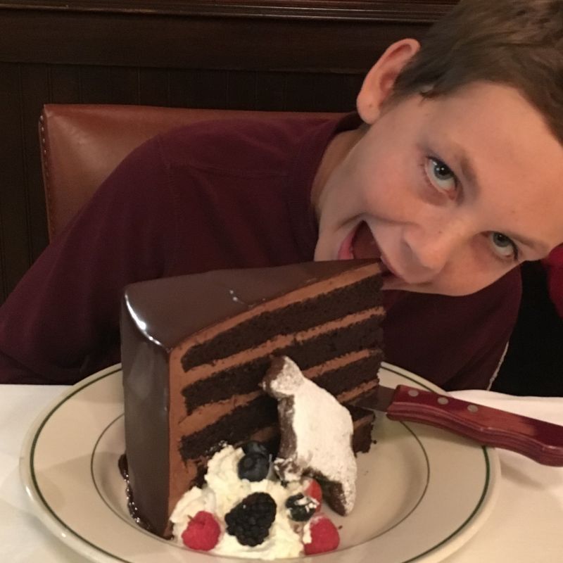 A young boy bites into a slice of chocolate cake