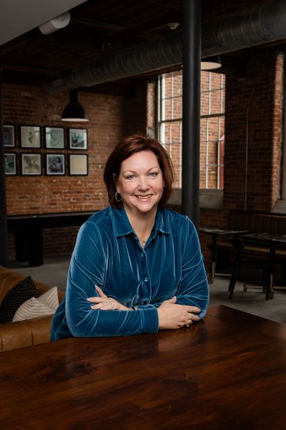 A woman is sitting at a table with her arms crossed and smiling.