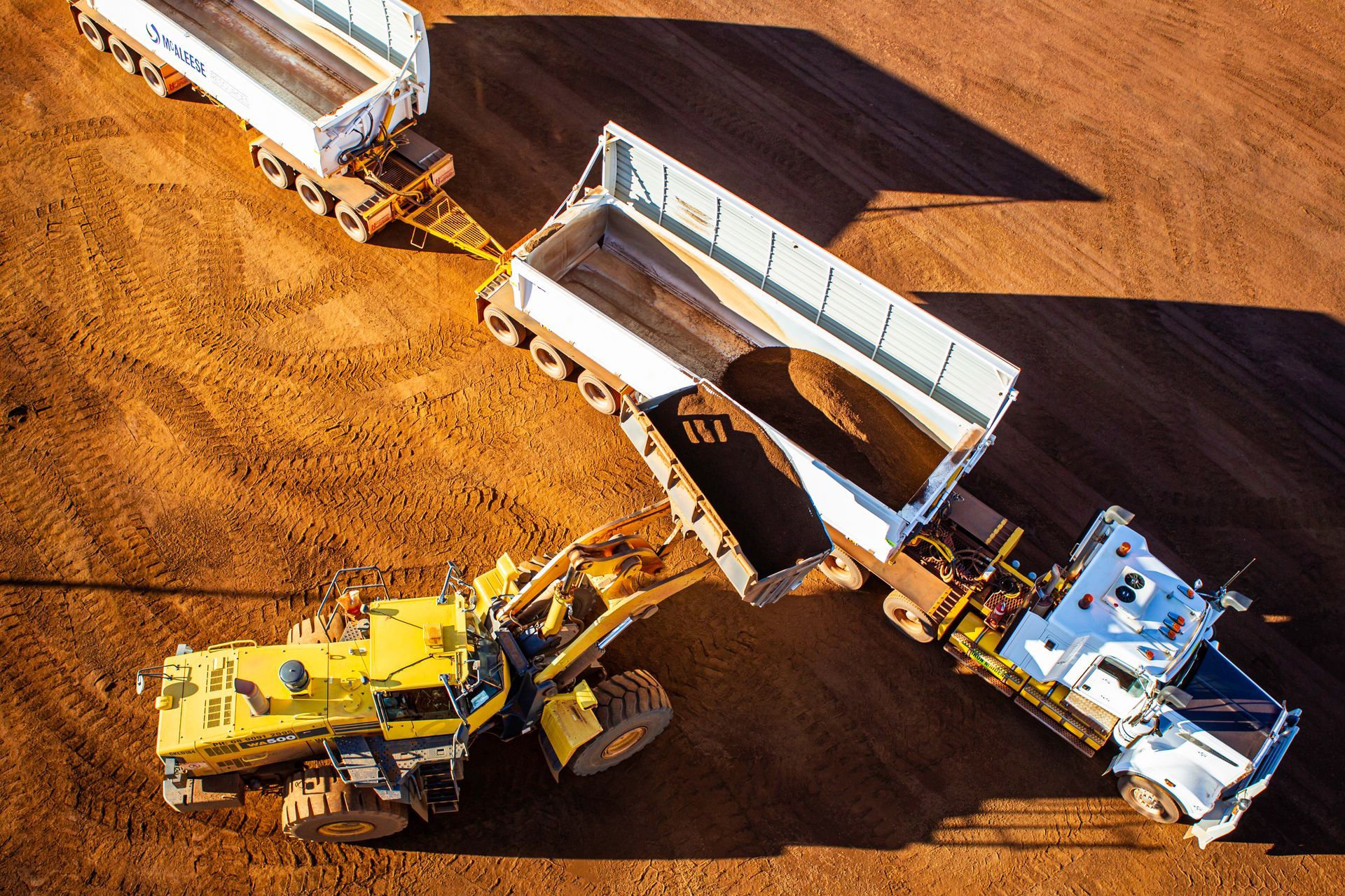 An aerial view of a bulldozer loading a dump truck with dirt
